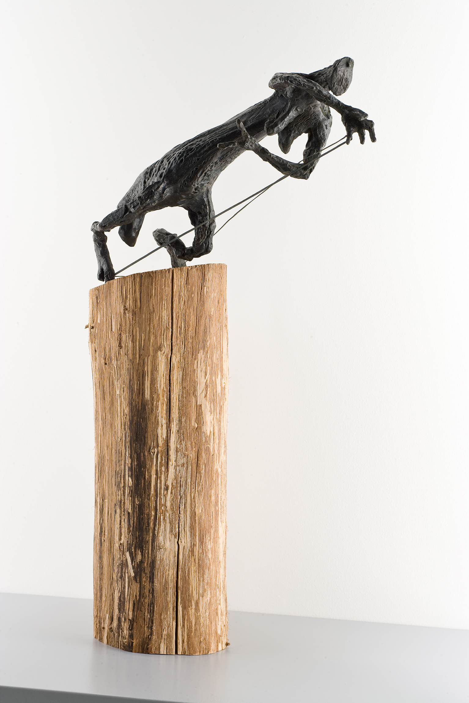 L'image représente une sculpture impressionnante. On peut voir une figure en bronze ou en métal, semblable à un animal, qui semble en mouvement, peut-être en train de courir ou de sauter. Cette figure est positionnée sur un socle en bois brut, qui contraste avec la finition lisse de la sculpture. Le bois et le métal créent une belle harmonie esthétique, mettant en valeur la dynamique de l'œuvre. L'ensemble évoque à la fois la force et la légèreté.