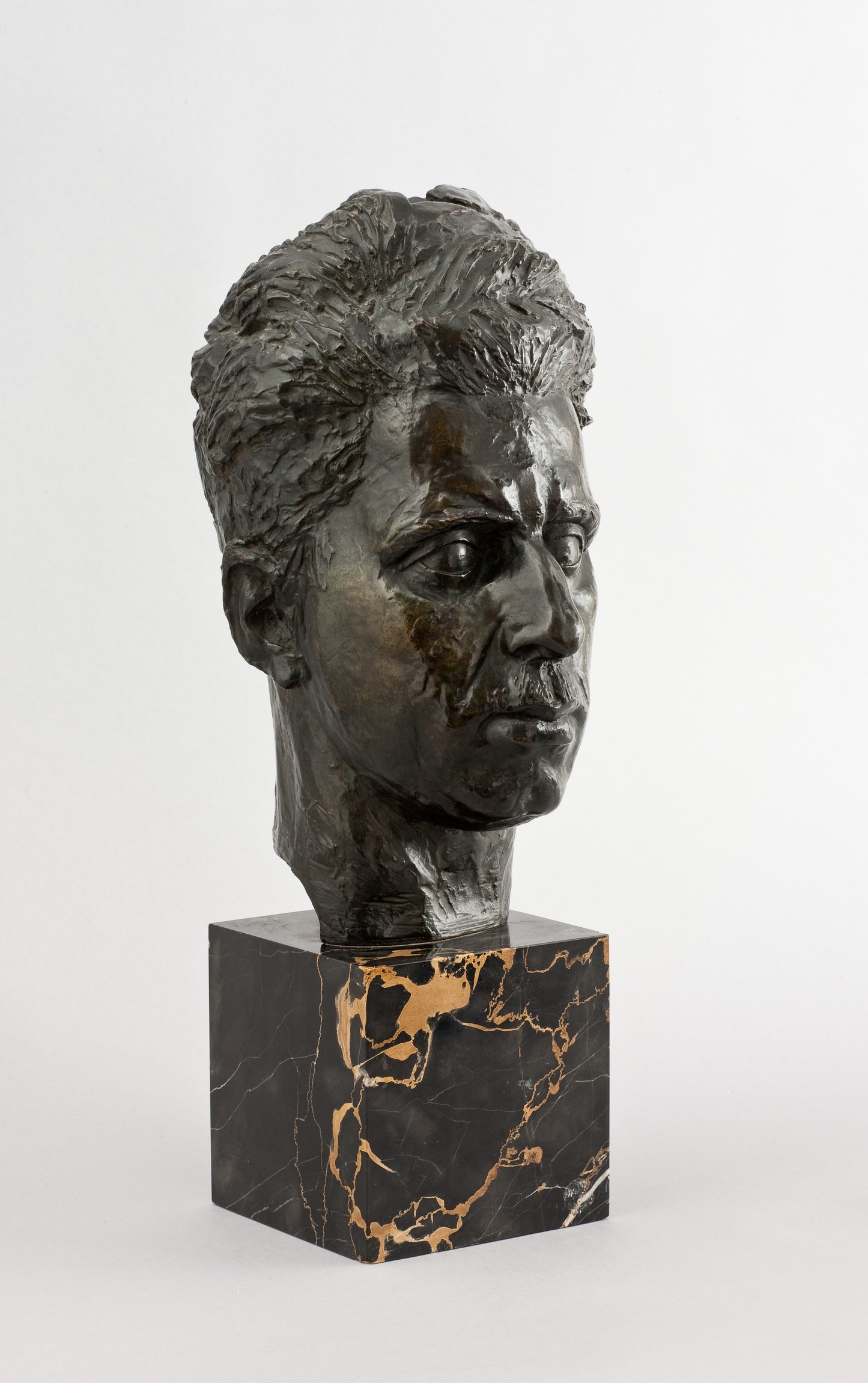 L'image présente une sculpture en bronze représentant un buste humain. Le buste, une fois poli, montre des détails réalistes du visage, y compris les traits et les expressions. La sculpture est montée sur une base en marbre noir avec des veines dorées, ce qui ajoute une touche d'élégance. L'ensemble dégage une impression à la fois artistique et intemporelle.