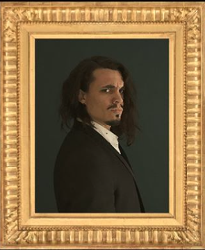 L'image représente un homme au style distinctif, portant un costume noir avec une chemise blanche. Il a des cheveux longs et légèrement ondulés, et son expression est à la fois sérieuse et intense. Le portrait est encadré dans un cadre doré, ajoutant une touche classique à l'ensemble. L'arrière-plan est simple, ce qui met en valeur le sujet.