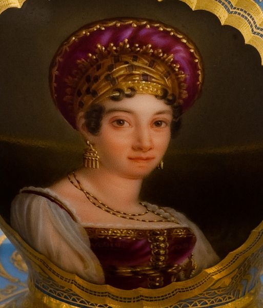 L'image présente un portrait féminin d'une femme au style historique, vêtue d'une robe élaborée avec des teintes de violet et d'or. Elle porte une coiffe ornée et des bijoux, notamment des boucles d'oreilles accrocheuses. Son expression est douce et elle regarde directement le spectateur, dégageant une certaine élégance et dignité. Le fond est décoré, ajoutant une touche artistique à l'ensemble du tableau.