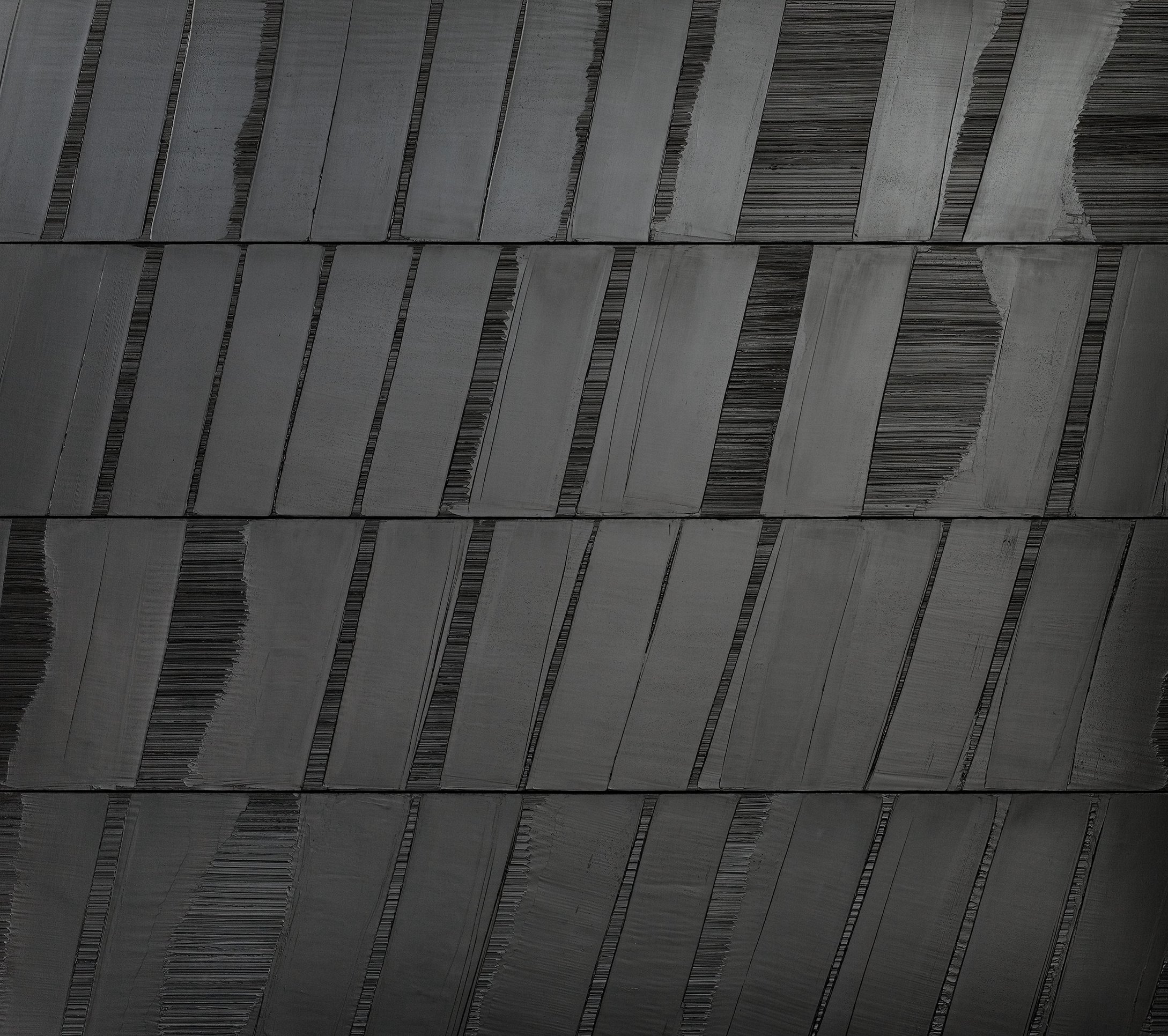 L'image montre une surface texturée composée de panneaux noirs disposés de manière oblique. Les panneaux présentent des variations de finition, certains ayant des lignes lisses tandis que d'autres semblent présenter des stries ou des motifs. L'ensemble crée un effet visuel intéressant avec des nuances de noir et des reflets subtils, suggérant à la fois modernité et élégance.