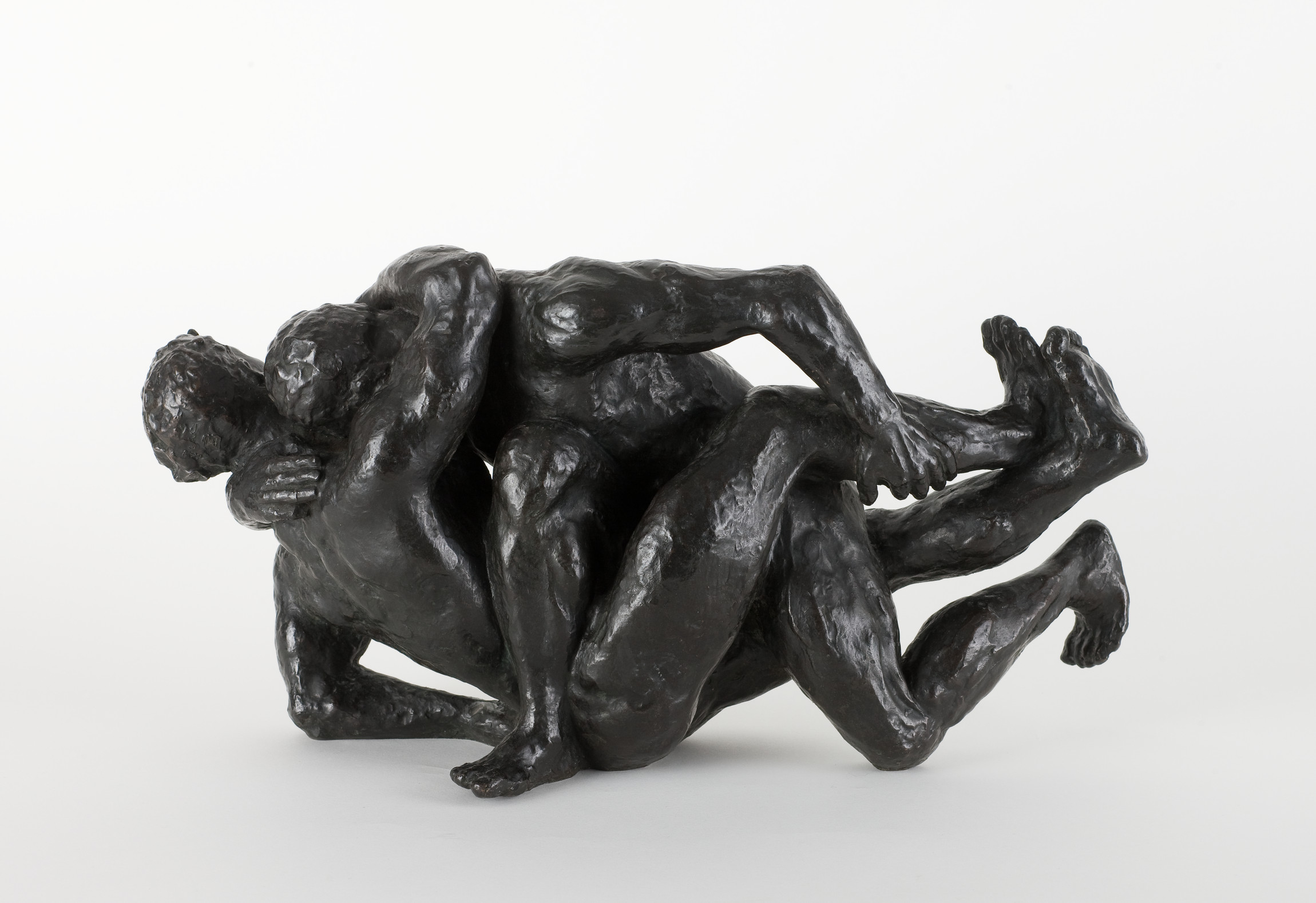 L'image représente une sculpture en bronze de deux figures humaines entrelacées dans une pose dynamique et expressive. Les corps semblent enchevêtrés, suggérant une interaction intime ou une danse. La surface de la sculpture est noire et mate, renforçant la profondeur des formes et des ombres. Les détails anatomiques sont accentués, mettant en évidence les muscles et les postures des personnages. L'œuvre évoque des thèmes tels que l'amour, la passion ou la lutte.