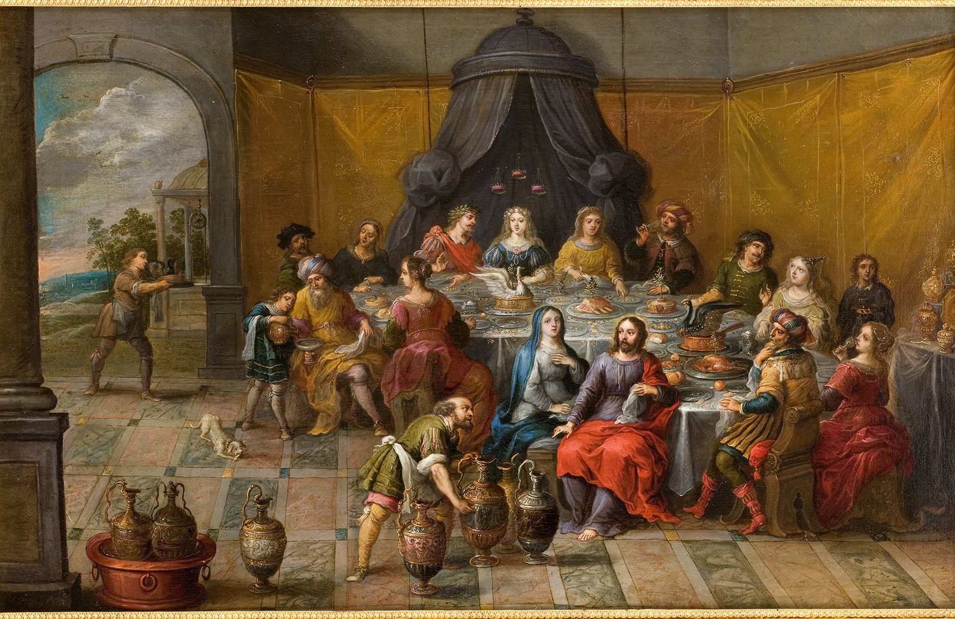 L'image représente une scène de banquet somptueux dans un cadre historique. Au centre, plusieurs convives sont assis autour d'une grande table chargée de mets délicats et de boissons. Les personnes sont vêtues de costumes d'époque colorés, certains portant des vêtements opulents. À gauche, un homme semble servir de la nourriture, tandis qu'un petit chien se trouve à ses pieds. En arrière-plan, on peut voir des arcades et des tentures dorées qui ajoutent à l'ambiance raffinée de la fête. L'ensemble dégage une atmosphère de célébration et de convivialité.