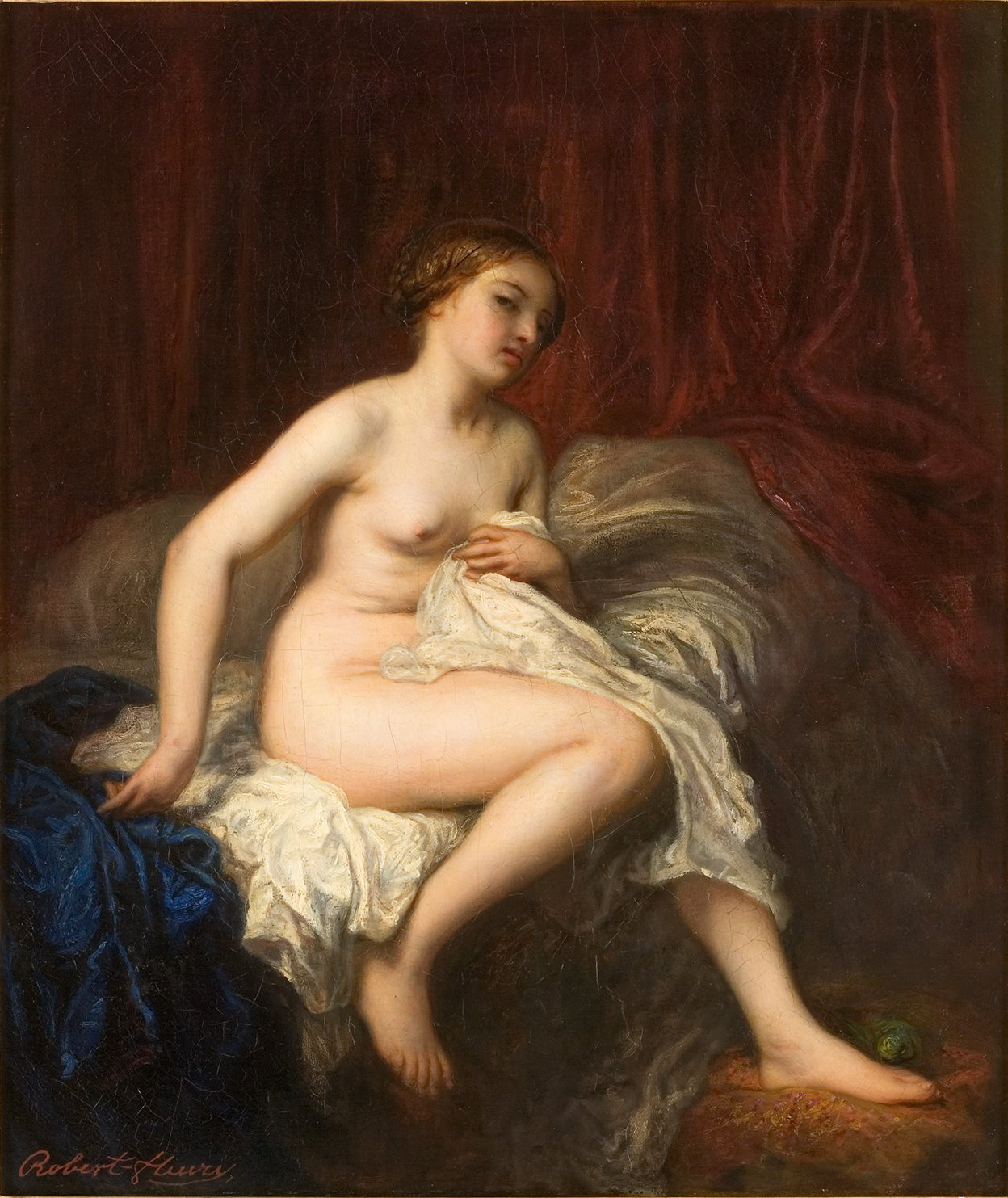 L'image représente une femme nue assise sur un divan. Elle est tournée légèrement sur le côté, son regard étant dirigé vers le bas. Ses cheveux sont châtains et tombent en boucles autour de son visage. Elle est entourée de drapés en tissu rouge et bleu qui créent un contraste riche avec sa peau. La lumière éclaire délicatement son corps, mettant en valeur ses formes. Cette œuvre semble évoquer la beauté et la sensualité à travers une composition classique.