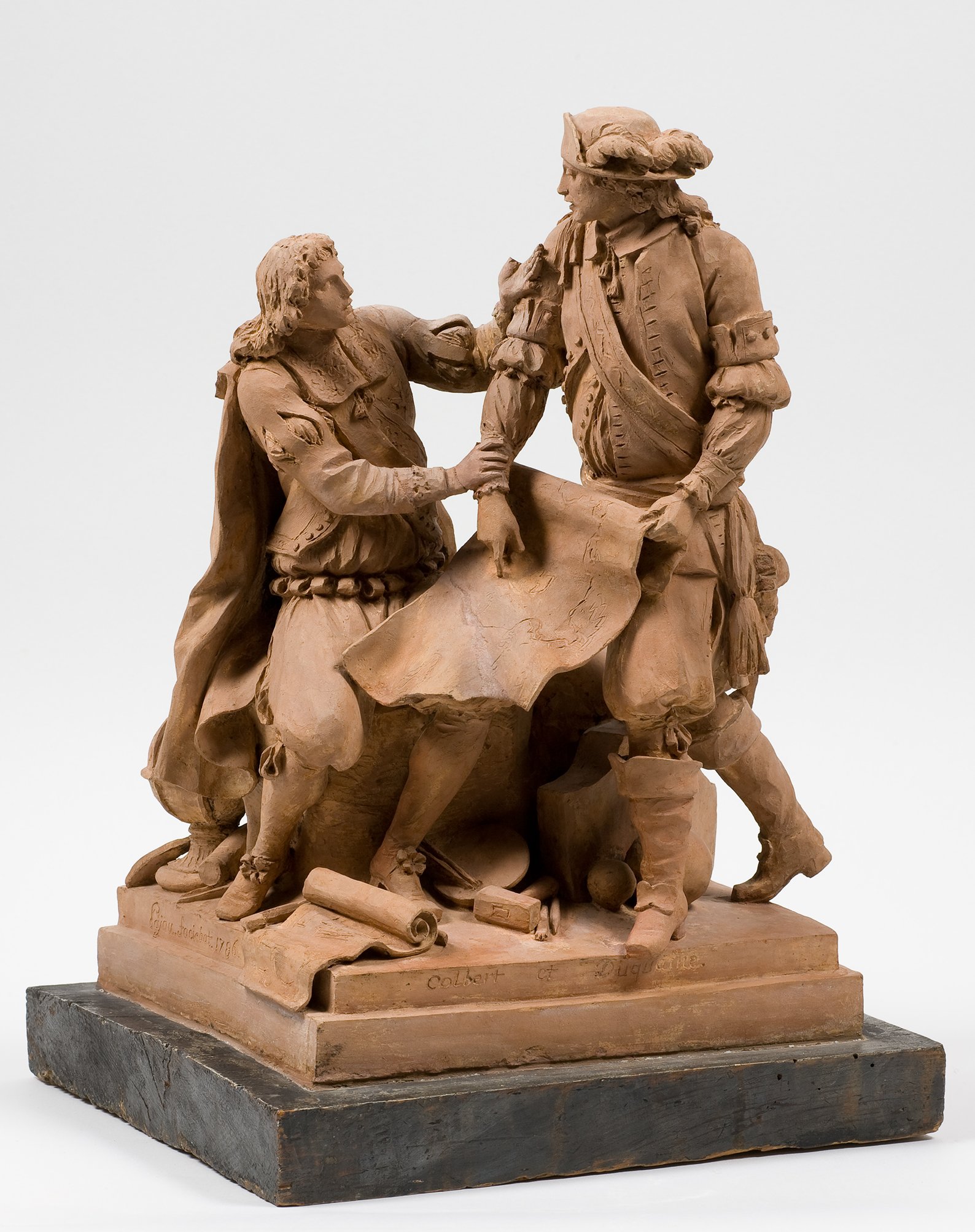 Cette image représente une sculpture en terre cuite montrant deux personnages en interaction. L'un semble tenir un document ou une carte, tandis que l'autre l'observe attentivement, peut-être en dialogue ou en discussion. Les vêtements des personnages évoquent une époque historique, avec des détails soignés qui mettent en valeur leur posture et leurs expressions. La sculpture est légèrement polie et repose sur une base noire, mettant en avant le travail artistique et les détails des figures.