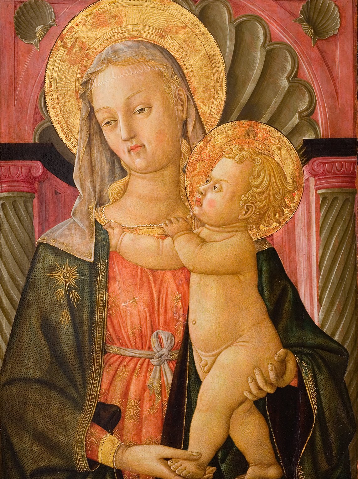 L'image représente une scène religieuse classique avec la Vierge Marie tenant l'enfant Jésus dans ses bras. Marie est dépeinte avec une expression douce, portant une robe ornée et un manteau sombre, ainsi qu'un voile sur la tête. L'enfant Jésus est nu, avec une expression curieuse, et porte une auréole dorée. L'arrière-plan est décoré de motifs architecturaux et de couleurs vives, ce qui ajoute à l'atmosphère sacrée de la peinture. Les détails, comme les halos dorés autour de leurs têtes, soulignent leur importance divine.