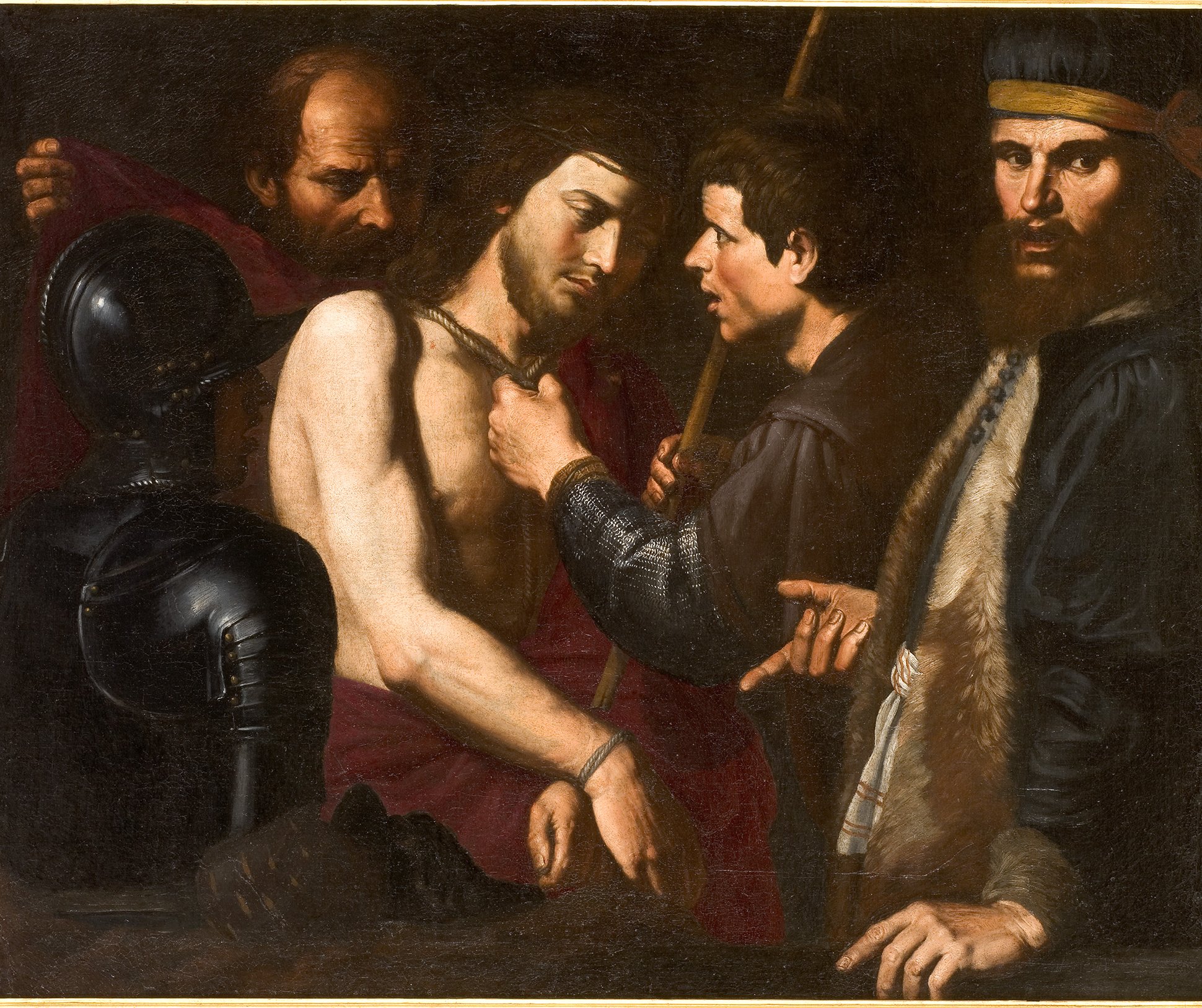 Cette image représente une scène de la passion du Christ, où Jésus est entouré de plusieurs personnages. Il est vêtu d'un drapé rouge et semble subir une interrogation ou un interrogatoire. Un homme à gauche porte une armure, tandis que d'autres personnages, aux expressions sérieuses, le regardent attentivement. L'un d'eux semble toucher la poitrine de Jésus, tandis qu'un autre regarde en arrière. La lumière dans l'œuvre met en avant les visages et les détails des vêtements, créant une atmosphère dramatique. Les couleurs sombres de l'arrière-plan contrastent avec les teintes plus claires des personnages.
