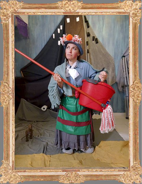 L'image montre une personne habillée de façon originale, portant un chapeau orné de fleurs. Elle tient un long bâton au bout duquel est fixé un seau rouge rempli d'eau et une serpillère. Son costume est composé de plusieurs couches de vêtements aux couleurs variées, avec une jupe et un manteau. L'arrière-plan est artistique, avec des éléments de décor qui évoquent un environnement créatif. L'ensemble donne une impression théâtrale et fantaisiste.