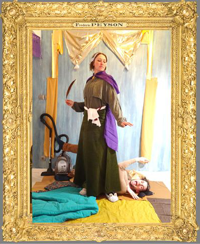 L'image semble représenter une scène théâtrale ou artistique. Au premier plan, on voit une femme vêtue d'une longue robe verte avec une étole violette, qui se tient dans une posture déterminée ou héroïque. Elle tient un objet qui ressemble à une lame. À ses pieds, une autre femme est allongée, ce qui suggère une dynamique entre les deux personnages. L'arrière-plan est décoré de tissus aux couleurs variées, et la scène est encadrée dans un cadre doré, ce qui donne un aspect de tableau. Ces éléments pourraient indiquer une mise en scène dramatique ou symbolique.