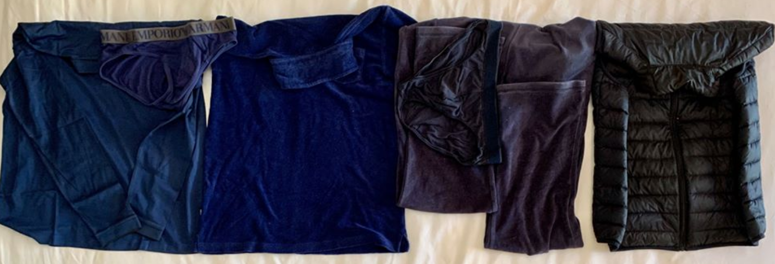 L'image montre plusieurs vêtements disposés en ligne sur une surface blanche. On y voit un haut bleu marine, un t-shirt, un sous-vêtement assorti, un pantalon ou un legging de couleur bleu foncé, et enfin un manteau léger ou une veste matelassée noire, qui a un col haut. Les textures des vêtements varient, allant du doux au matelassé.