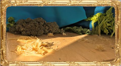 L'image présente une composition de légumes, avec du brocoli et des feuilles de légumes, sur une surface en bois. On peut également apercevoir des morceaux de fromage râpé qui sont dispersés au sol. La lumière éclaire doucement la scène, créant des ombres et des reflets, tandis qu'un tissu bleu est visible en arrière-plan. L'ensemble donne une impression de fraîcheur et de naturel.