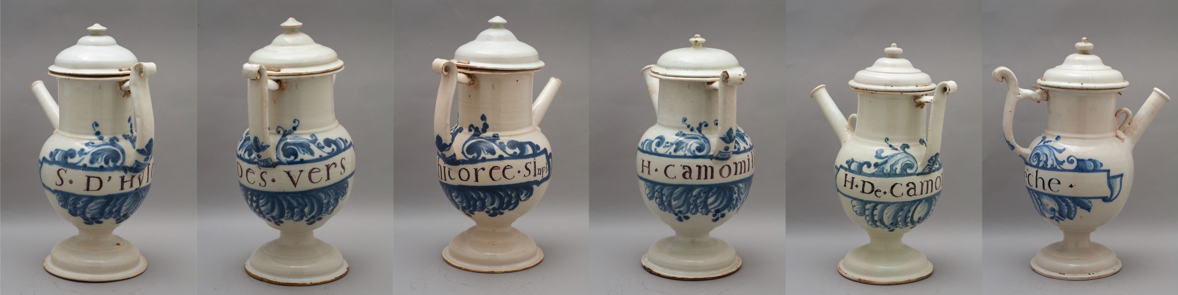 L'image présente une série de pots ou de récipients en faïence, typiquement décorés avec des motifs en bleu sur fond blanc. Chaque pot possède un couvercle et une anse. Les inscriptions, bien que partiellement visibles, semblent indiquer des noms ou des lieux, suggérant qu'ils pourraient avoir eu une fonction particulière, comme celle de contenir des boissons. La forme est élégante et traditionnelle, témoignant d'un style artisanal. Les motifs de décoration ajoutent une touche artistique à l'ensemble.