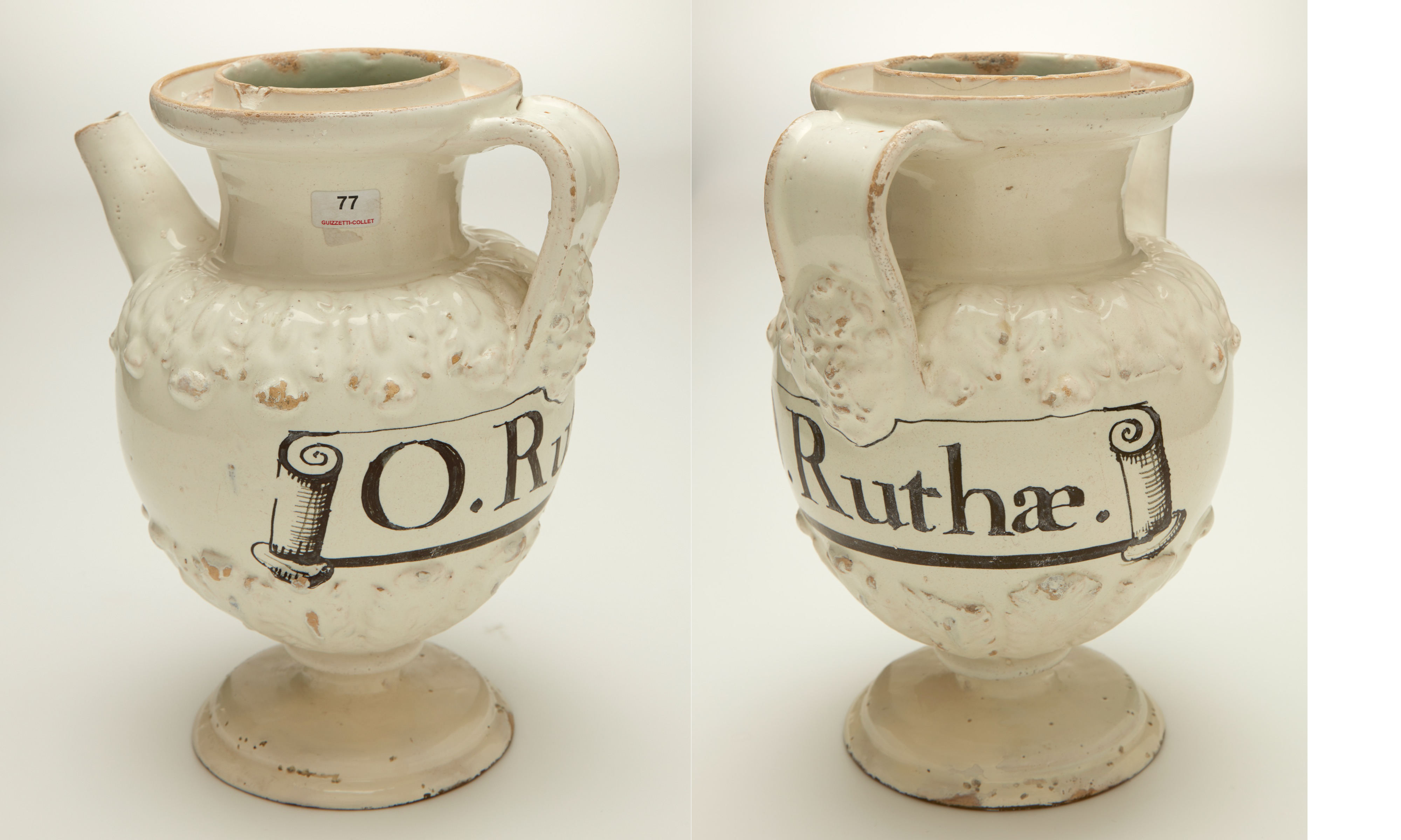 L'image montre un pichet en céramique de forme arrondie, avec une anse sur le côté. Le pichet est décoré d'un motif en relief, et a une finition de couleur crème. Sur le devant, on peut voir un texte inscrit qui semble lire "O. Ruthæ", probablement en lettres noires et stylisées. L'objet a une base large et est légèrement évasé vers le haut, ce qui lui confère une allure élégante et ancienne.