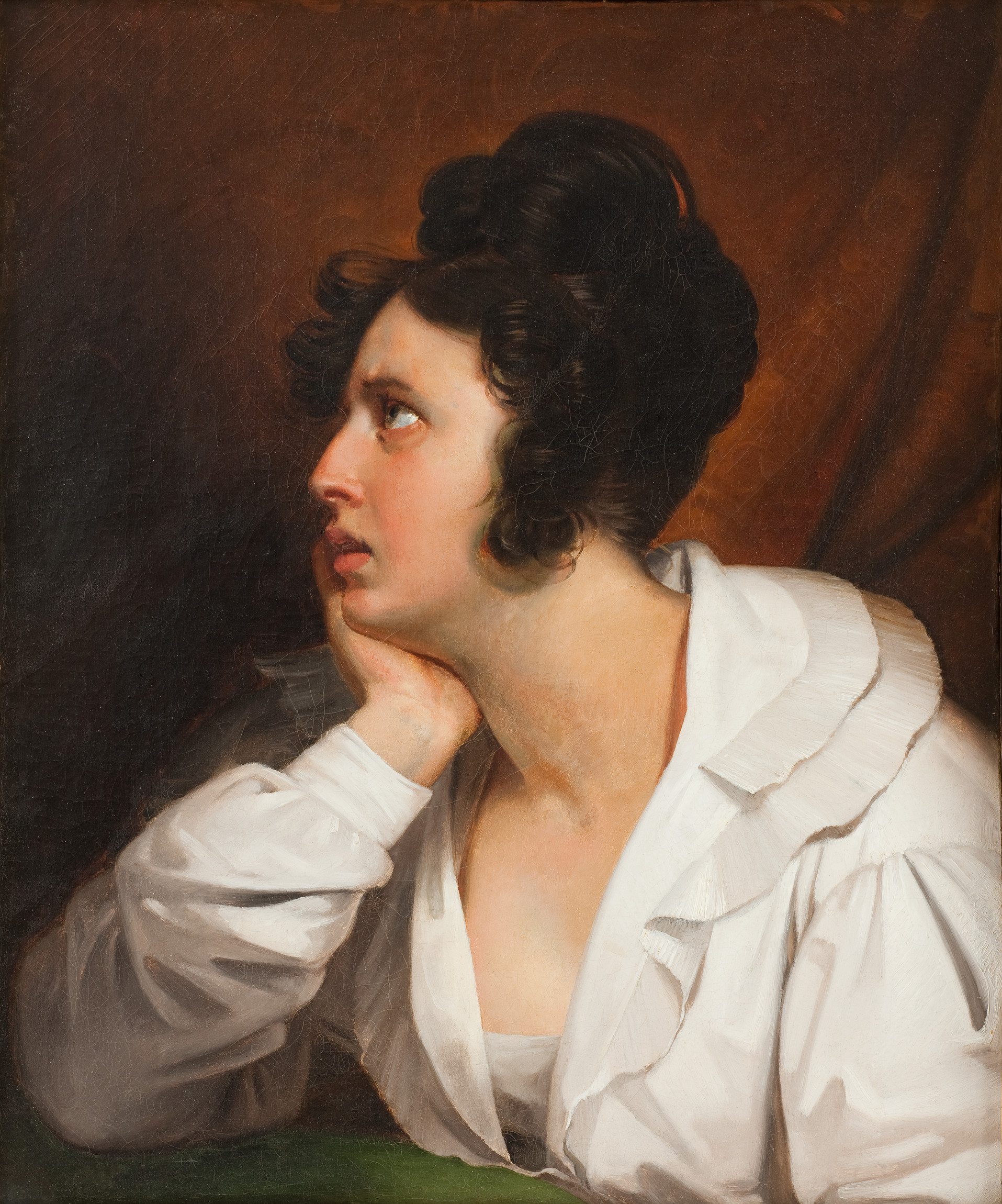 L'image représente une femme ayant une expression pensive. Elle est de profil, la tête légèrement inclinée vers la gauche, avec une main posée sur son menton. Ses cheveux sont bruns et coiffés en boucles, et elle porte une blouse blanche avec des volants au col. L'arrière-plan est sombre, ce qui met en valeur son visage et son regard expressif. La lumière accentue ses traits, créant un contraste marqué avec l'ombre environnante. L'ensemble évoque une atmosphère de contemplation ou de mélancolie.