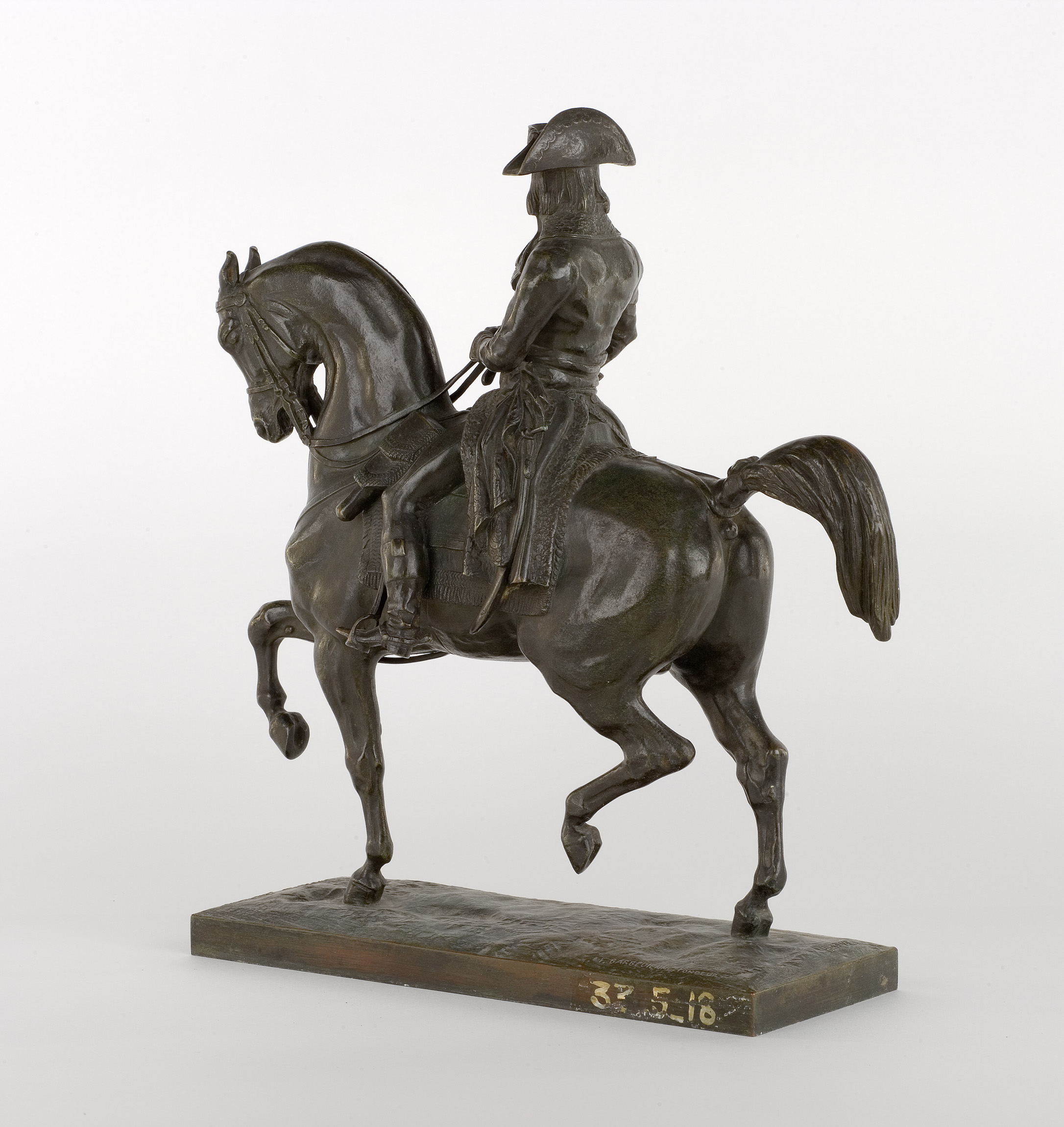 Cette image représente une sculpture en bronze d'un cavalier, probablement un militaire, monté sur un cheval. Le cavalier est en position dominante, se tenant droit sur sa monture. Il porte un uniforme militaire et un chapeau, ce qui suggère qu'il pourrait représenter une figure historique importante. La sculpture est finement détaillée, mettant en avant le mouvement dynamique du cheval et la posture fière du cavalier. La base de la sculpture est également visible, supportant l'ensemble de l'œuvre.