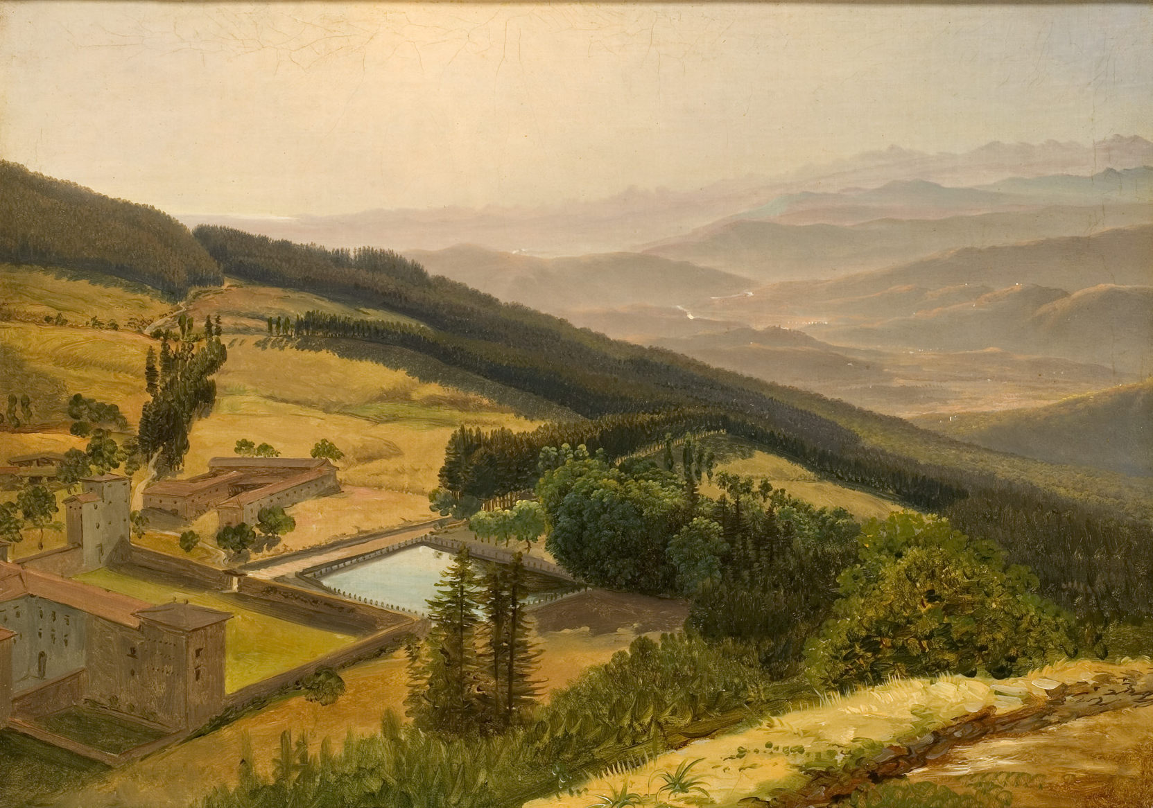 L'image montre un paysage paisible avec des collines verdoyantes s'étendant à perte de vue. Au premier plan, on aperçoit un bâtiment de style ancien entouré d'arbres et de végétation. Une étendue d'eau, probablement un étang, est visible, reflétant la lumière du soleil. À l'arrière-plan, les montagnes se dessinent dans la brume, ajoutant une touche de mystère au paysage. La lumière douce suggère une ambiance calme et sereine, typique d'un matin ou d'un début de soirée.