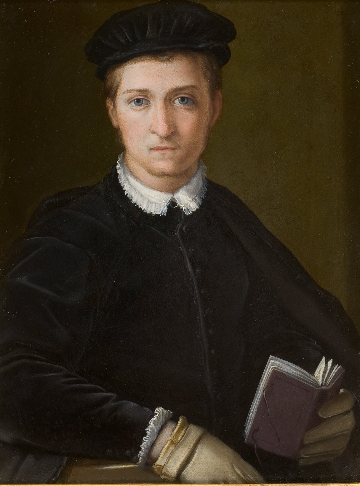 L'image représente un jeune homme en portrait. Il porte un chapeau noir et une tenue sombre, ornée d'un col blanc qui contraste avec le reste de ses vêtements. Il tient un petit livre dans sa main, ce qui suggère qu'il pourrait être un intellectuel ou un érudit. Son expression est sérieuse et son regard est direct, créant un lien avec le spectateur. L'arrière-plan est simple, ce qui met en valeur le sujet du portrait.