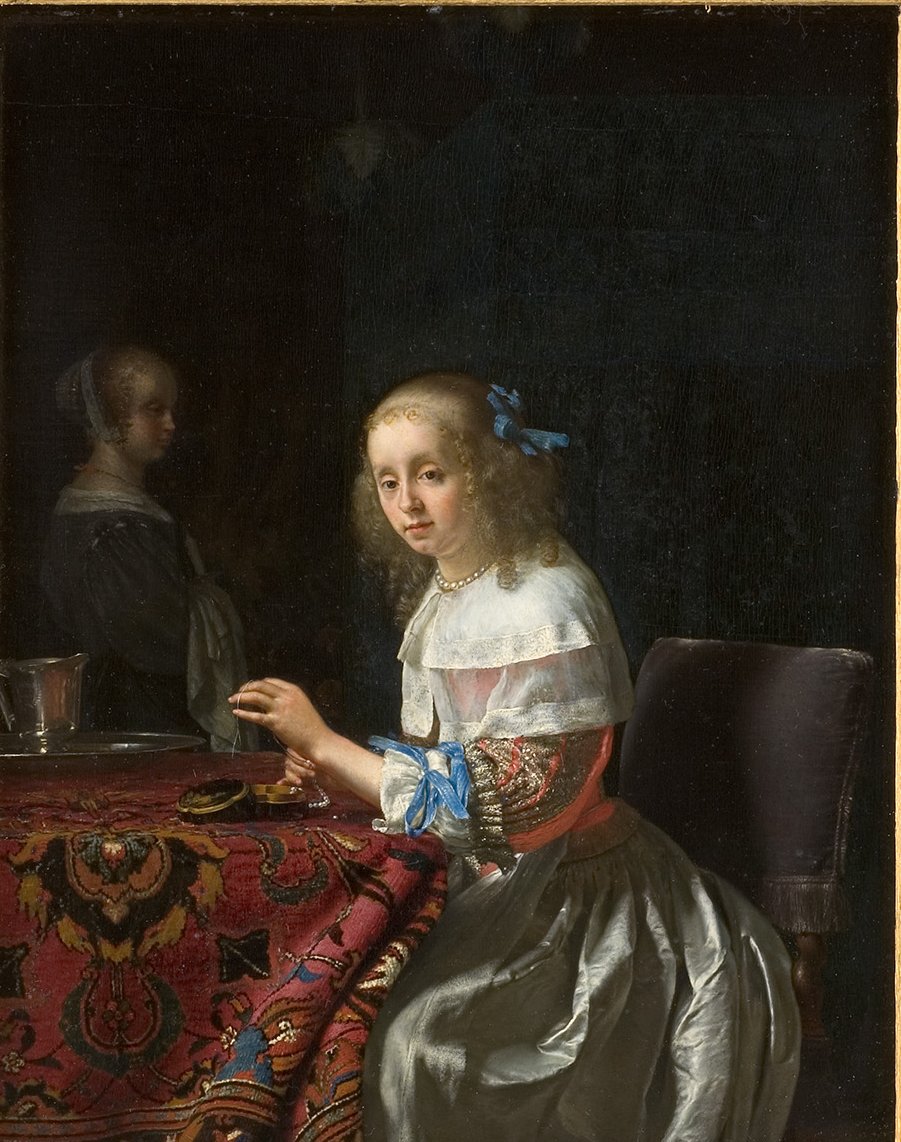 L'image représente une scène intime avec deux jeunes femmes. La première, au premier plan, est assise à une table recouverte d'une nappe colorée. Elle porte une robe élégante avec des détails en soie et un nœud bleu dans ses cheveux. Son expression est douce et pensive, alors qu'elle regarde vers le spectateur. À l'arrière-plan, une autre femme est visible, légèrement floue, ce qui donne une impression de profondeur à la composition. L'éclairage met en valeur les textures et les couleurs des vêtements ainsi que la richesse de l'environnement, créant une ambiance calme et réfléchie.