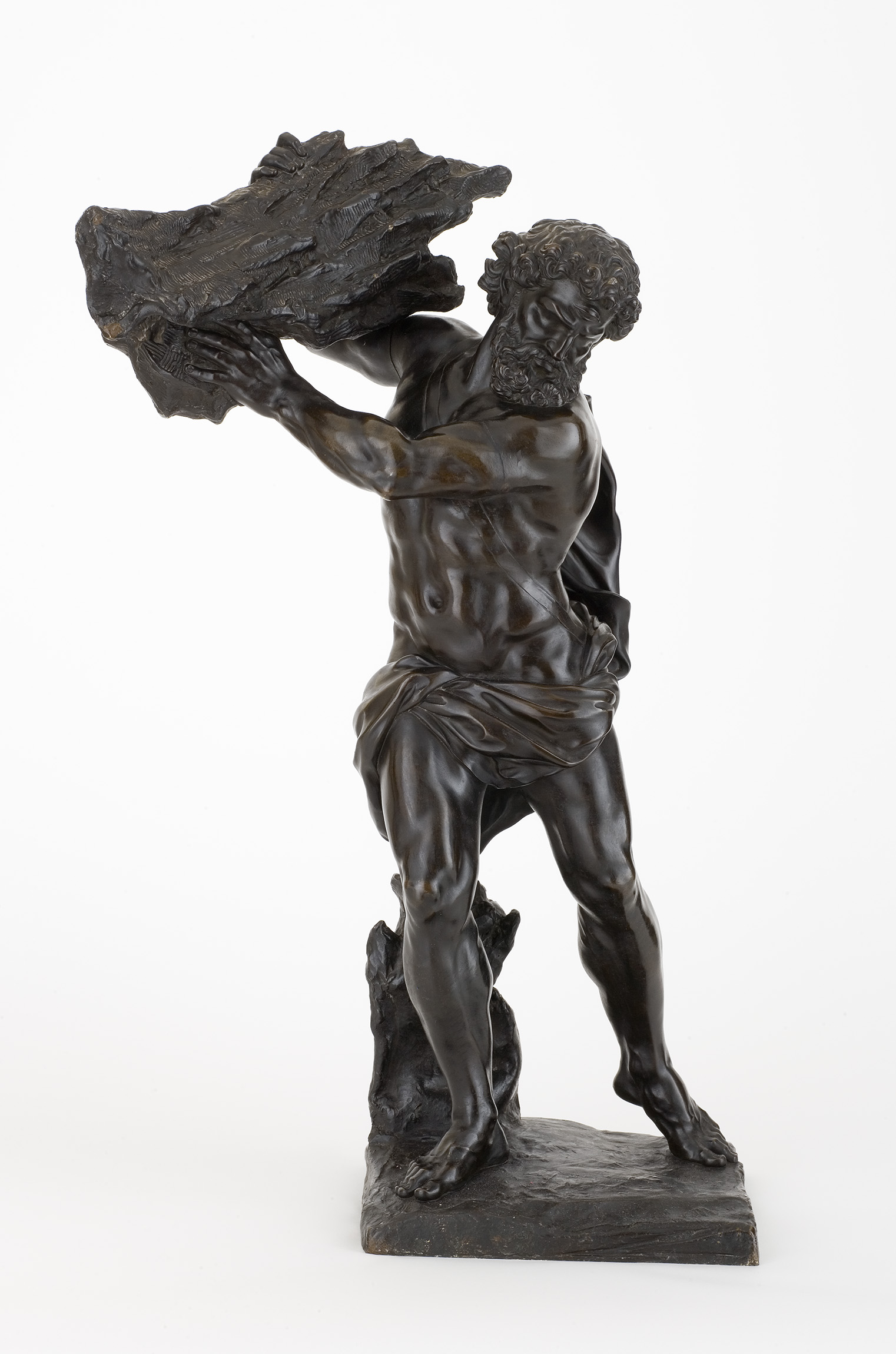 L'image représente une sculpture en bronze d'un homme nu, portant un lourd rocher. Il a une barbe et des cheveux ondulés, et son corps est en position dynamique, suggérant un effort physique intense. Ses muscles sont bien définis, accentuant la force qu'il déploie. Son expression faciale est déterminée, ce qui renforce l'idée de puissance et de lutte. La base de la sculpture est texturée et semble représenter un environnement naturel, ajoutant à l'impression de mouvement et de défi.