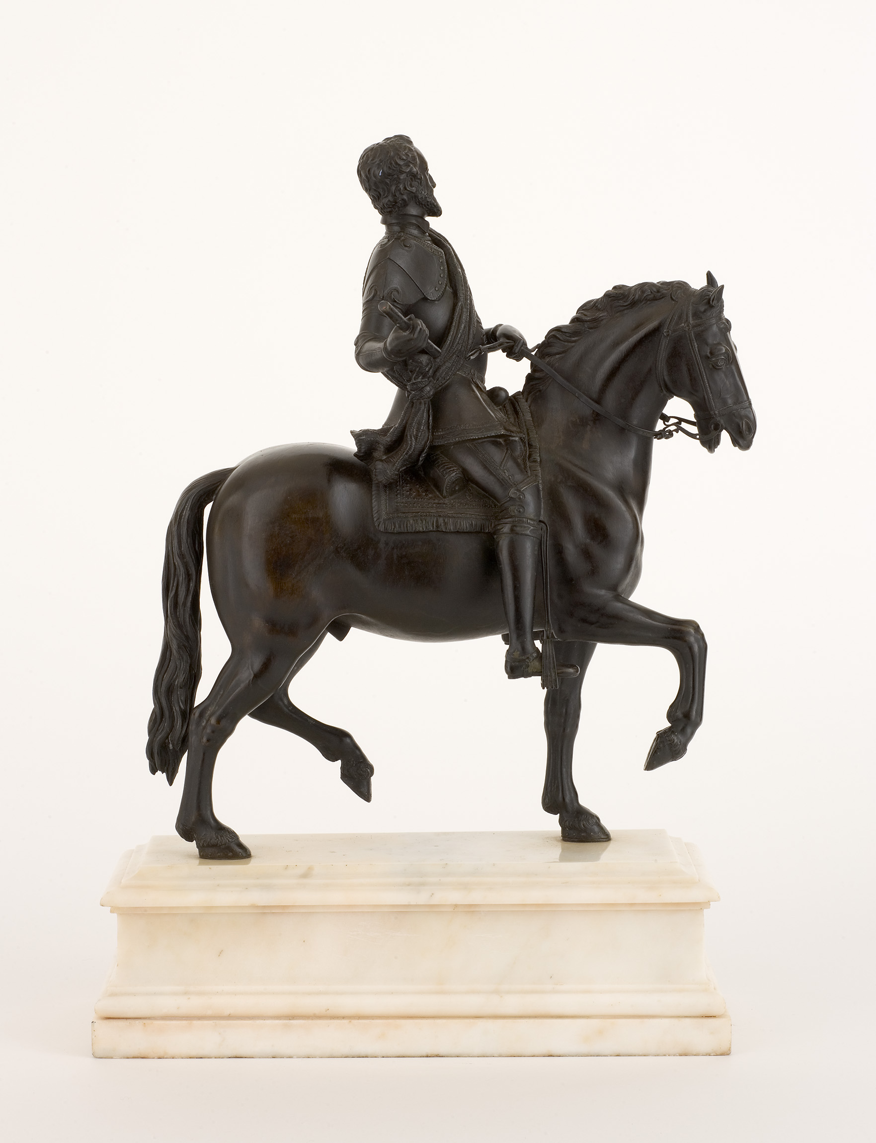 L'image représente une sculpture en bronze d'un cavalier sur son cheval. Le cavalier est habillé dans une tenue historique, probablement d'une époque aristocratique, et il semble tenir quelque chose dans sa main. Le cheval est représenté avec une posture dynamique, levant une patte. La sculpture repose sur une base en marbre, offrant un contraste élégant avec le bronze. L'ensemble dégage une impression de grandeur et de mouvement.