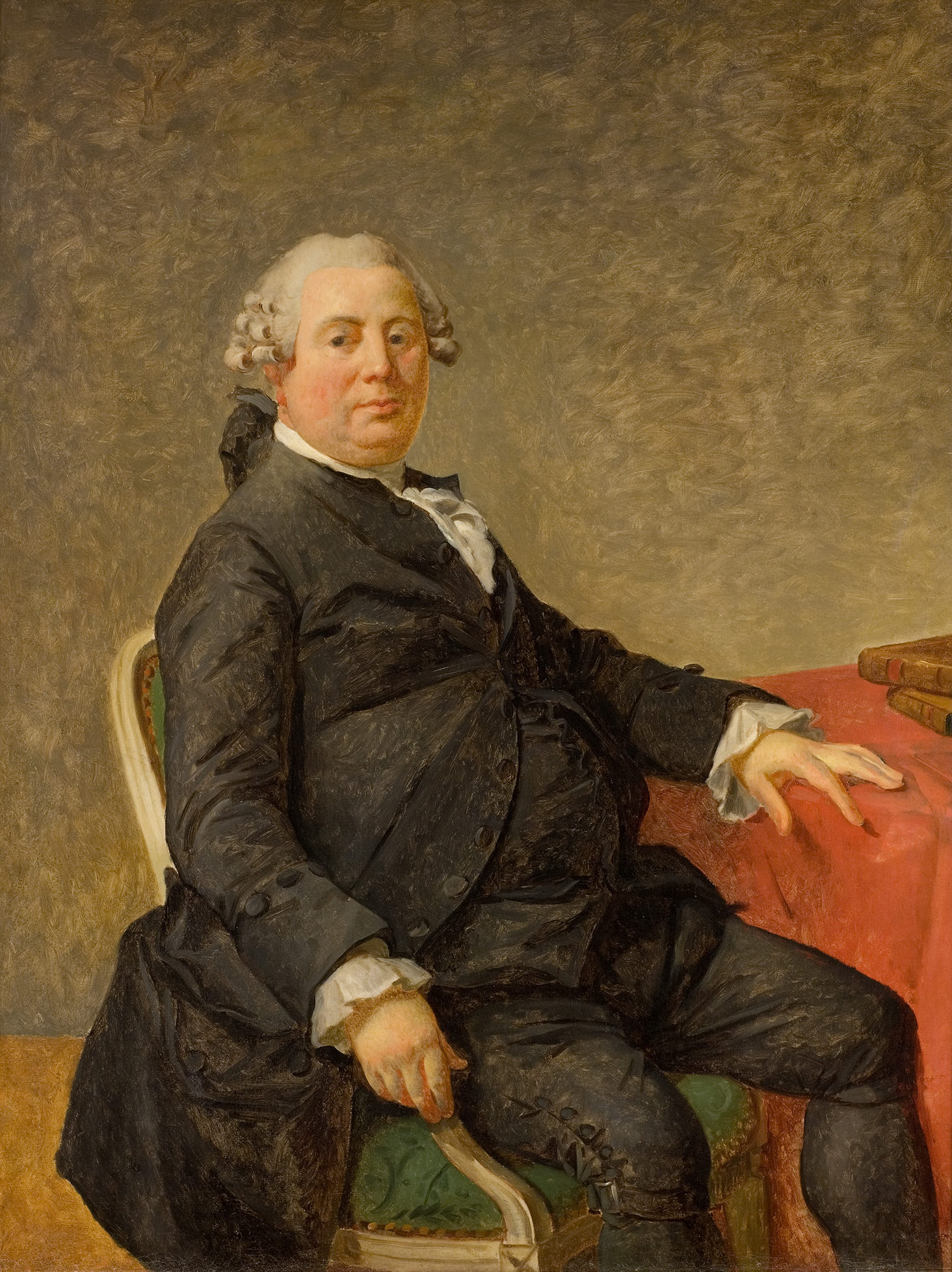 L'image représente un homme assis à une table, vêtu d'un costume sombre avec une chemise blanche. Il a des cheveux frisés et porte une expression calme. La pièce semble être éclairée de manière douce, et le fond est d'une couleur beige uniforme. La table à laquelle il est assis est couverte d'une nappe rouge, et quelques objets semblent y être posés. L'homme semble appartenir à une époque historique, faisant penser au XVIIIe ou XIXe siècle.