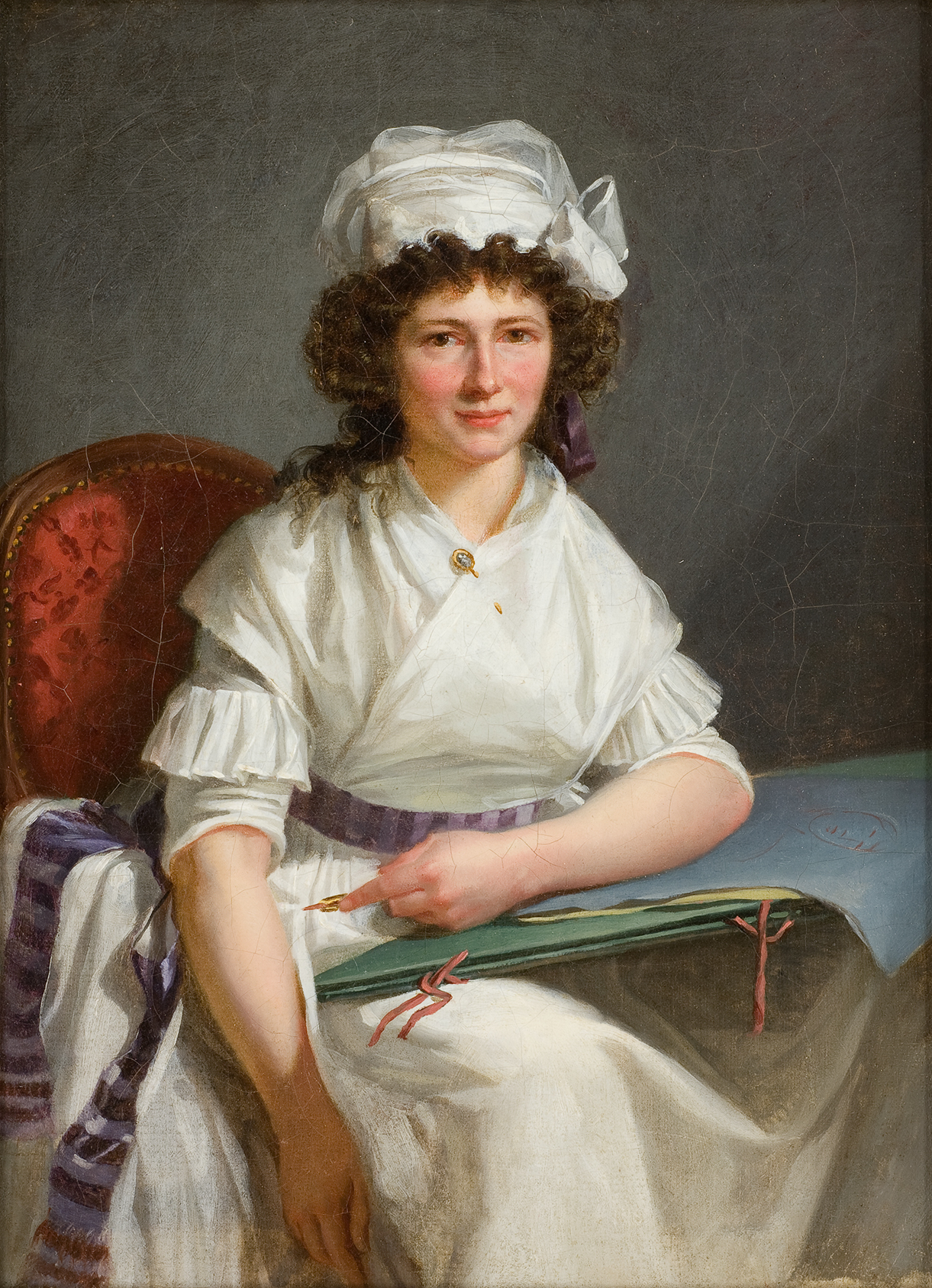 L'image représente un portrait d'une femme assise, vêtue d'une robe blanche avec des détails texturés. Elle porte un chapeau blanc et a des cheveux bouclés. La femme est placée sur une chaise rouge et tient un grand cahier ou un livre ouvert sur ses genoux. Son expression est douce et engageante, et elle semble regardant le spectateur avec un léger sourire. L'arrière-plan est plutôt sobre, mettant en valeur le sujet du tableau.