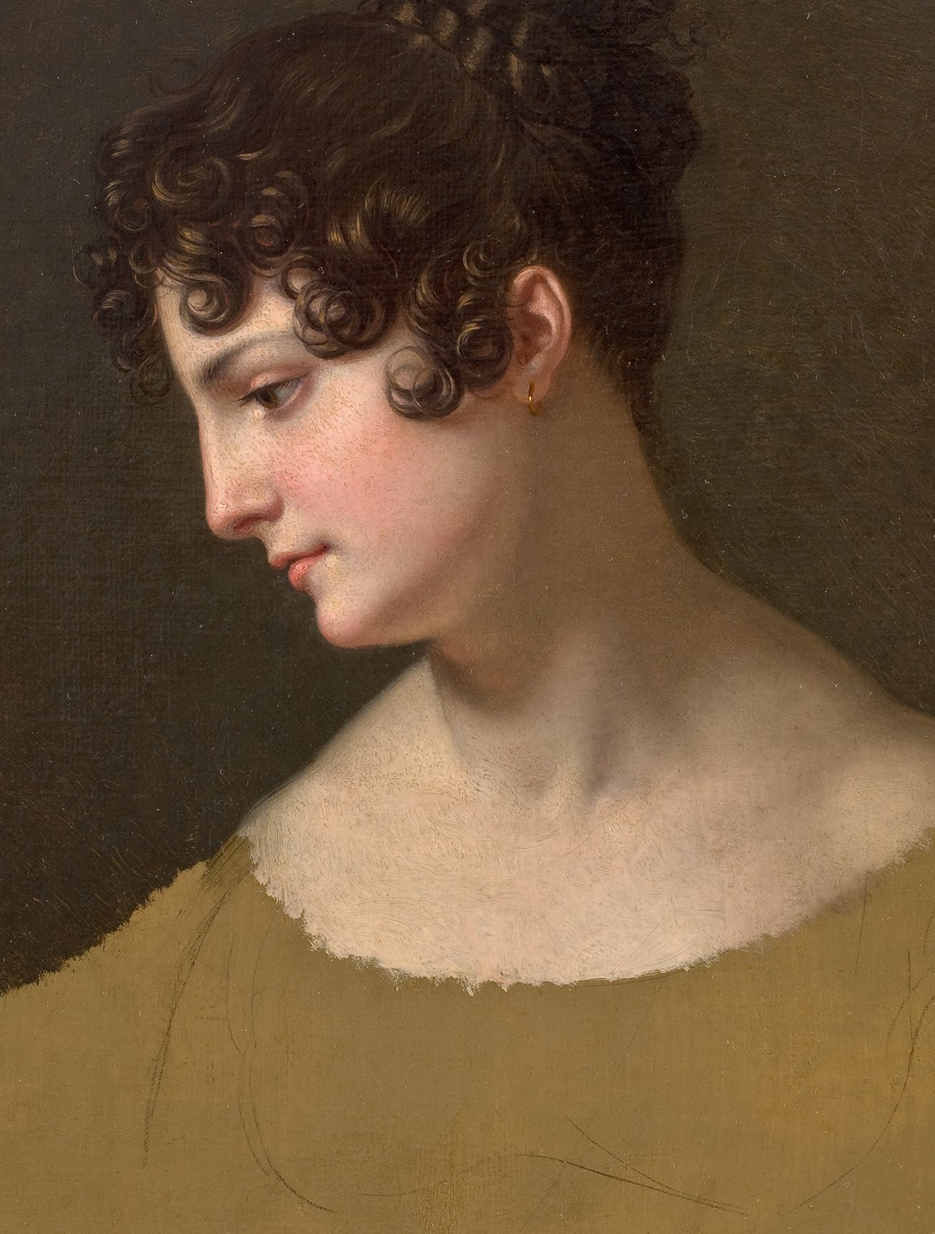 L'image présente un portrait d'une femme avec des cheveux bouclés et un profil délicat. Elle a une expression douce, avec des traits fins et une peau claire. La lumière met en valeur son visage, créant un contraste avec l'arrière-plan sombre. La femme porte une blouse à épaules dénudées de couleur beige, ajoutant à l'élégance de sa pose.