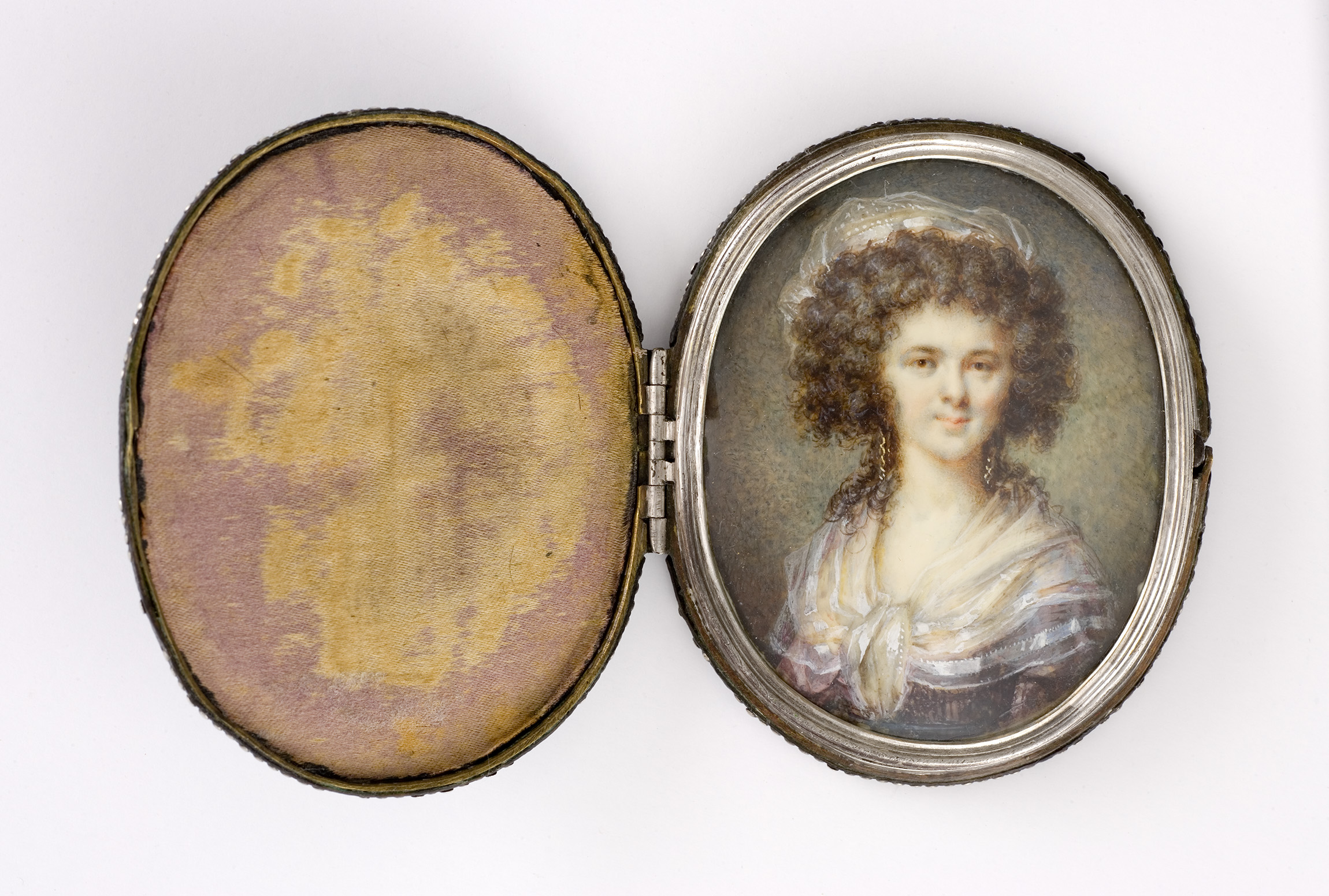 L'image montre un médaillon ouvert contenant un portrait. Le portrait représente une femme avec des cheveux bouclés et un sourire doux. Elle porte un vêtement élégant, peut-être une robe avec un col. L'arrière-plan du médaillon est orné d'un tissu d'une couleur douce, qui contraste avec l'image. Le cadre du médaillon est en métal, ajoutant une touche de sophistication à l'ensemble.