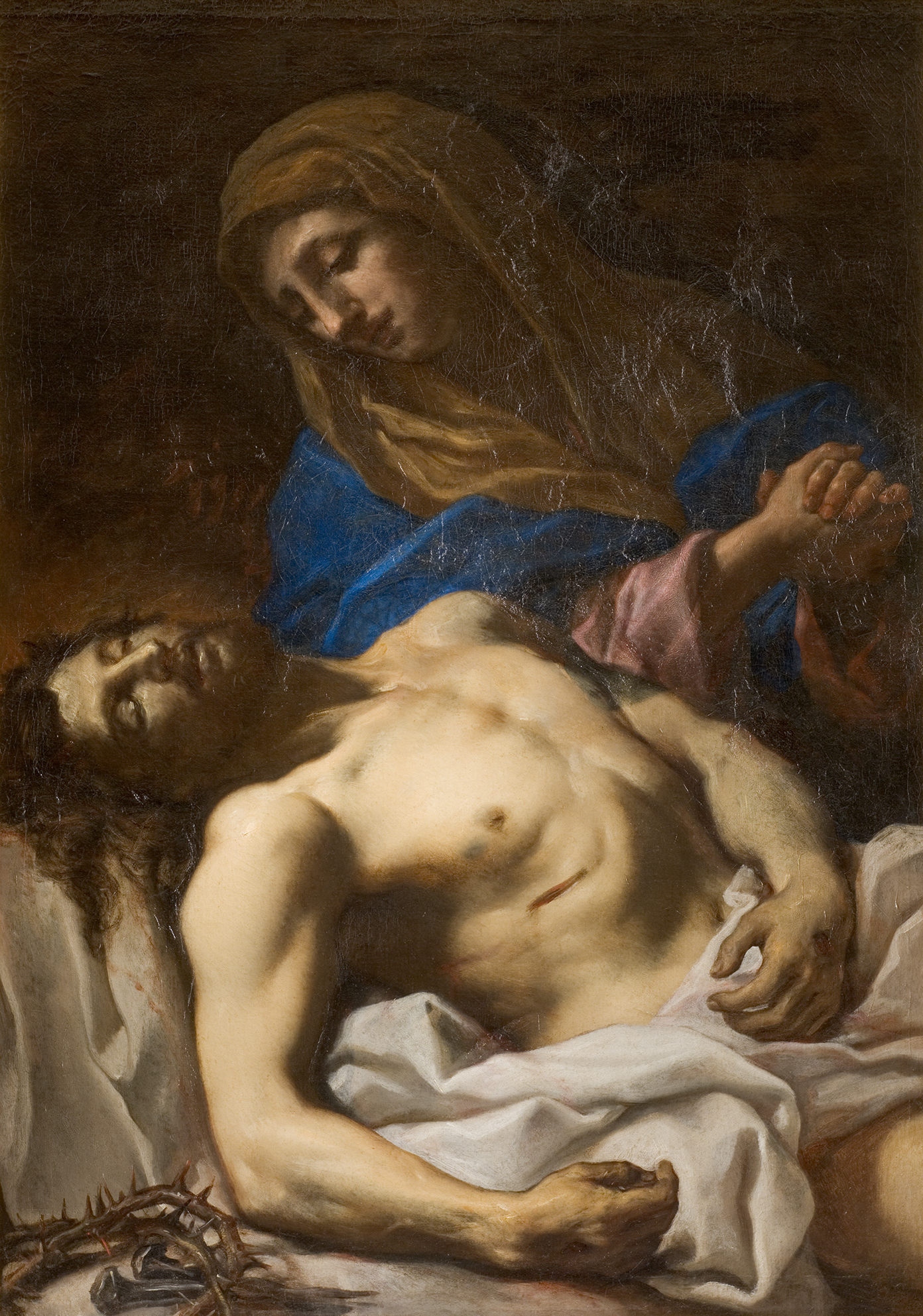 Cette image représente une scène poignante de la Vierge Marie tenant le corps du Christ après la crucifixion. Marie, vêtue d'un manteau bleu et d'une robe rose, exprime une profonde tristesse et compassion. Le corps du Christ, allongé sur un drap blanc, est dépouillé de sa croix, avec une couronne d'épines à ses pieds. La lumière met en valeur les détails des visages et des drapés, créant une atmosphère émotive et de recueillement.