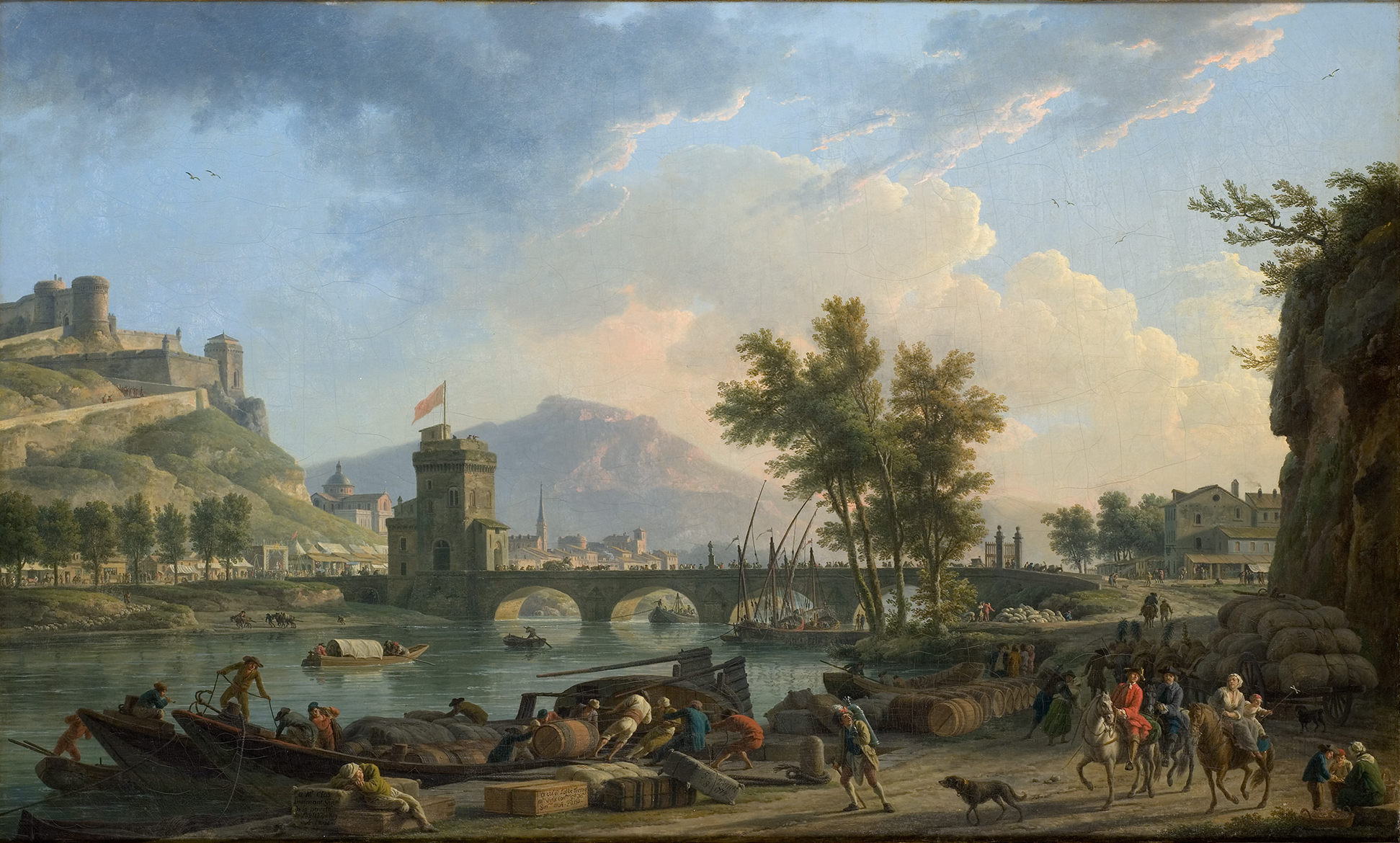 L'image représente un paysage fluvial animé, avec un pont qui traverse une rivière. À gauche, plusieurs bateaux sont amarrés, où des hommes s'affairent à charger et à décharger des marchandises, comme des tonneaux. Sur la rive, des personnages se déplacent, certains à pied et d'autres à cheval. En arrière-plan, on aperçoit des collines et des montagnes, ainsi que des bâtiments, dont une tour qui semble faire partie d'une fortification. Le ciel est clair, avec quelques nuages, et l'ensemble dégage une atmosphère tranquille et pittoresque.