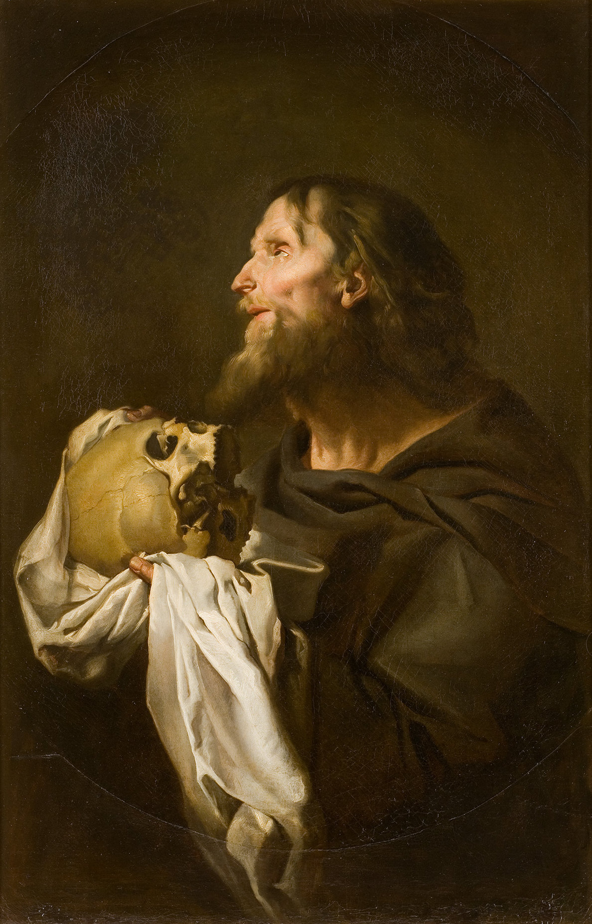 L'image représente un homme âgé, probablement un saint ou un ermite, tenant un crâne dans une main et un morceau de tissu dans l'autre. Il a une longue barbe et des cheveux crépus, et son expression semble contemplative, voire mélancolique. Le fond est sombre, ce qui accentue la lumière qui éclaire son visage et l'objet qu'il tient, créant une atmosphère dramatique et introspective. Ce tableau évoque des thèmes de mortalité et de réflexion sur la vie.