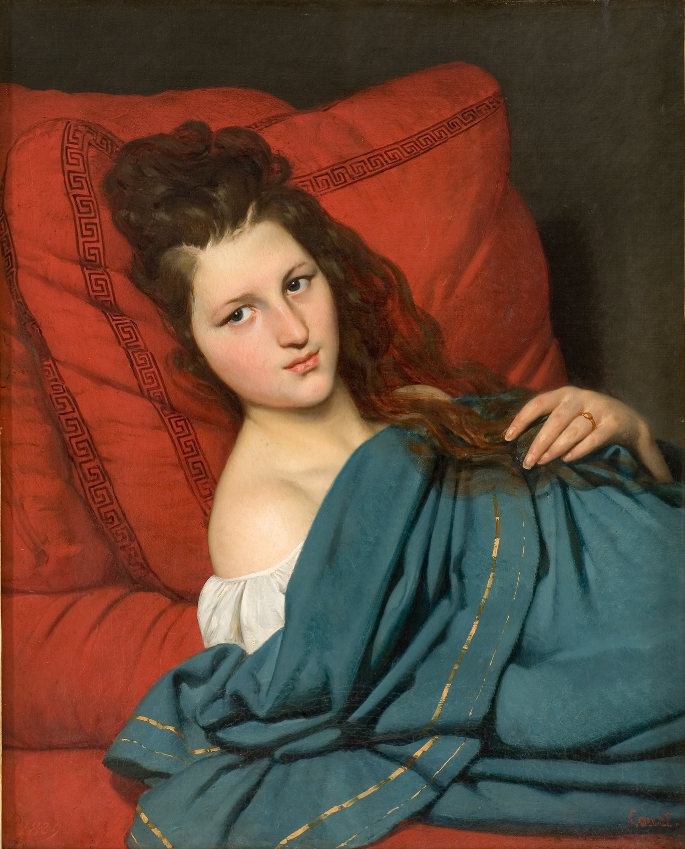 L'image représente une jeune femme allongée sur un canapé. Elle est vêtue d'une chemise blanche, tandis qu'elle est partiellement recouverte d'une couverture de couleur turquoise avec des motifs dorés. Son regard est pensif, et elle se trouve dans une position détendue mais réfléchie. Le fond est sombre, ce qui met en valeur la lumière sur son visage et les couleurs vives de ses vêtements et du canapé rouge sur lequel elle repose. Les détails de son expression et de sa posture évoquent une ambiance à la fois intime et introspective.