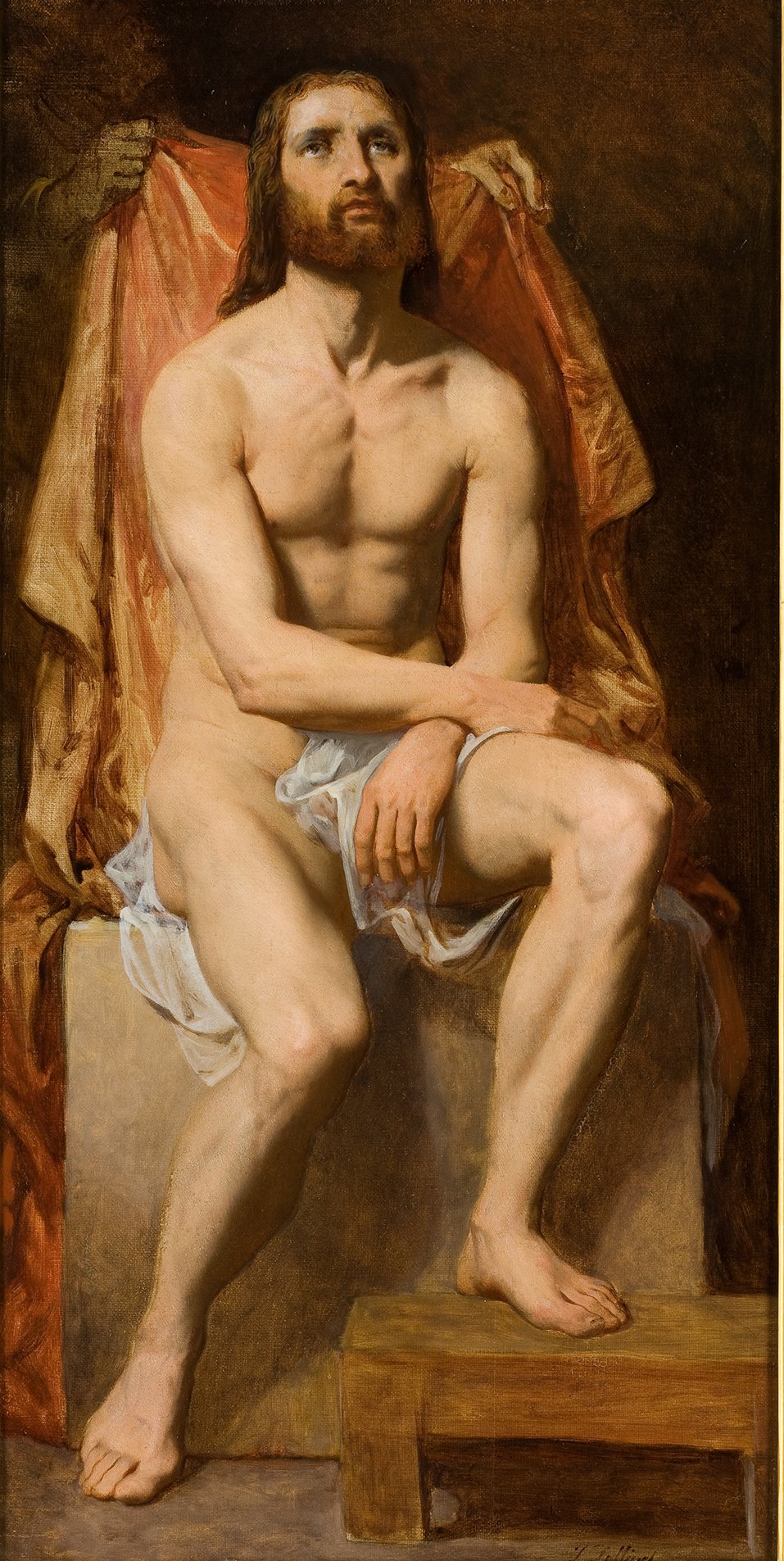 L'image représente un homme nu, assis sur un tabouret en bois. Il a des cheveux longs et une barbe et semble contemplatif. Son corps est légèrement tourné, avec une posture qui évoque la sérénité. Il est partiellement drapé dans un tissu léger autour des hanches. En arrière-plan, un rideau drapé de couleur rougeâtre ajoute de la profondeur à la composition. L'éclairage met en valeur les contours de son corps, créant un contraste avec l'obscurité environnante. La scène dégage une atmosphère à la fois calme et mystique.