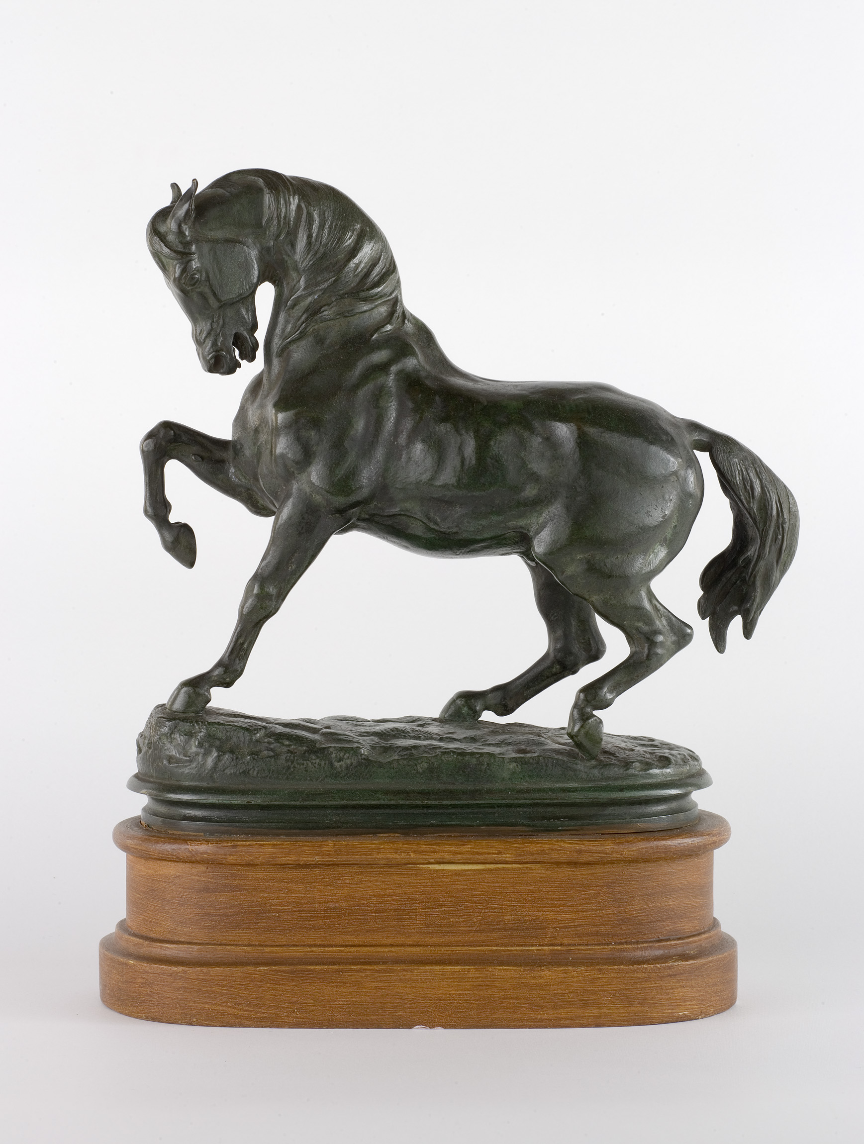 L'image montre une sculpture en bronze représentant un cheval en position dynamique, levant une patte avant. Le cheval est détaillé, avec une musculature bien définie et une crinière fluide. La sculpture repose sur une base en bois polie, qui ajoute une touche d'élégance à l'ensemble. Les lignes de l'œuvre évoquent le mouvement et la grâce de l'animal, soulignant le savoir-faire artistique.