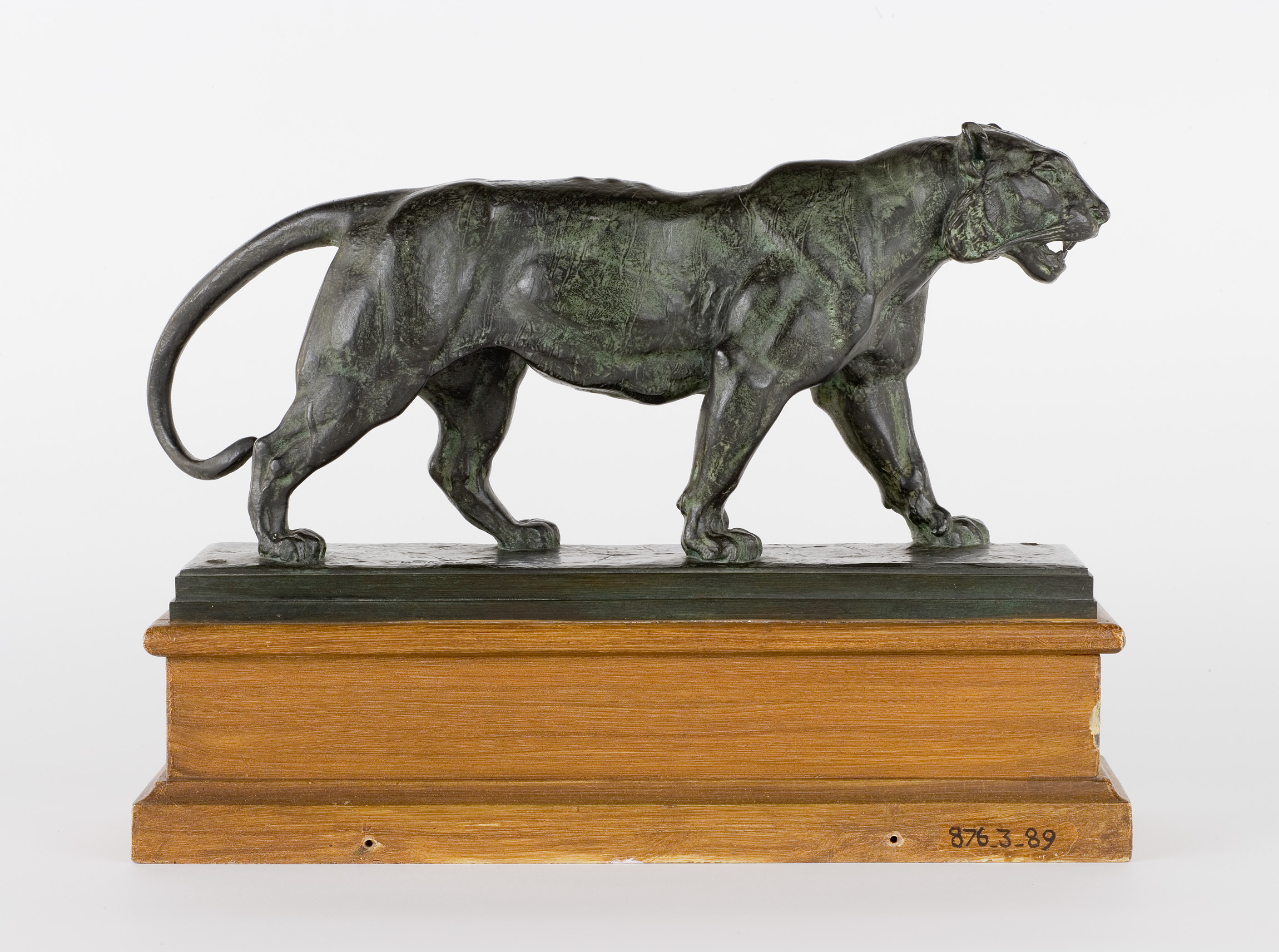 L'image représente une sculpture en bronze d'un tigre marchant. Le tigre est dépeint dans une position dynamique, avec son corps en mouvement et un regard féroce. La sculpture est posée sur une base en bois, qui met en valeur l'œuvre. Les détails de la fourrure et des muscles sont soigneusement travaillés, donnant vie à l'animal. Cette œuvre évoque la puissance et la grâce du tigre.