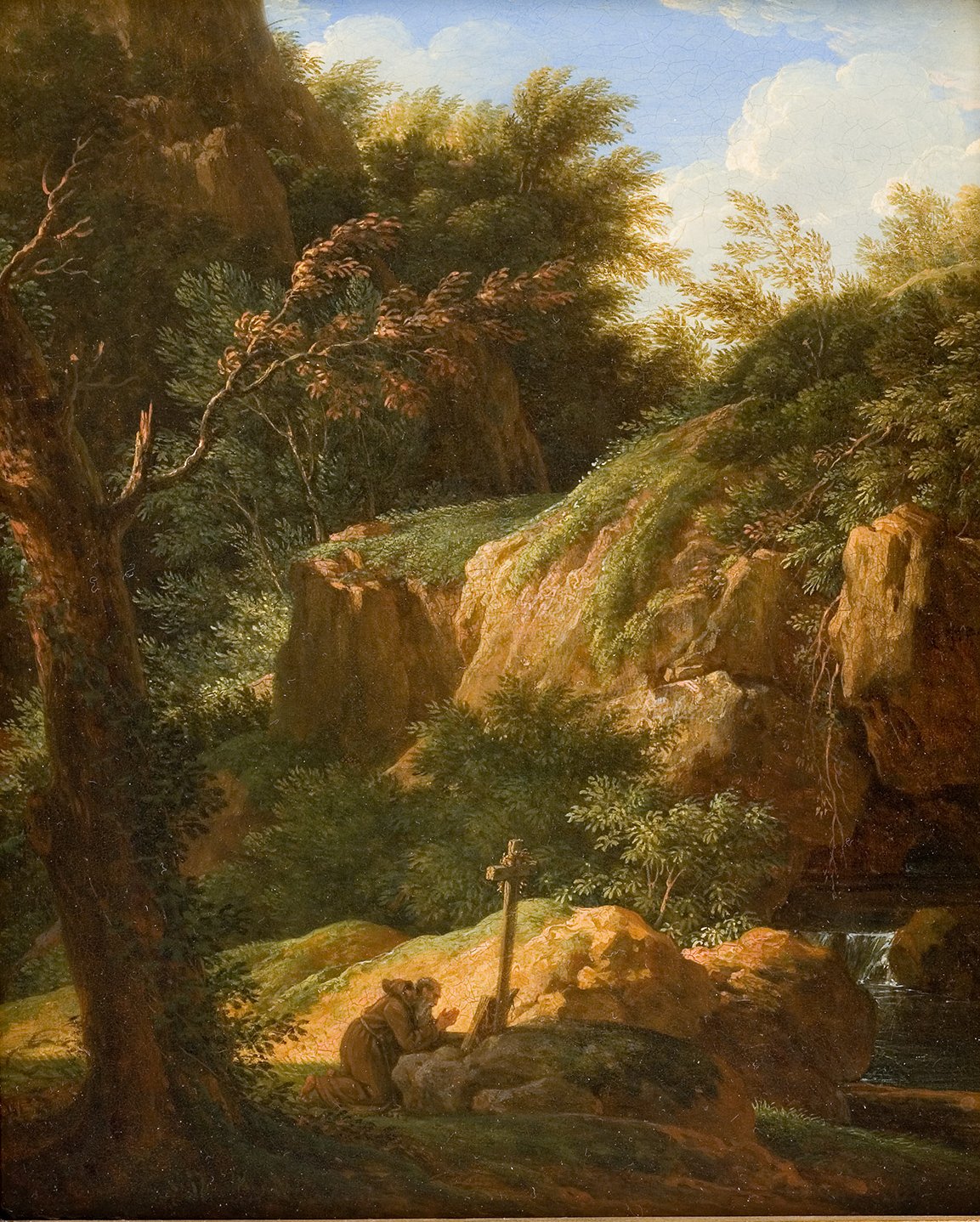 L'image représente un paysage naturel paisible, avec des rochers imposants et une végétation luxuriante. À gauche, on aperçoit un arbre dépouillé et, au premier plan, un homme agenouillé près d'une croix en bois, semblant méditer ou prier. L'arrière-plan est dominé par des collines verdoyantes et un ciel partiellement nuageux, créant une atmosphère sereine et contemplative. Un petit ruisseau semble couler à proximité, ajoutant une dimension apaisante au tableau.