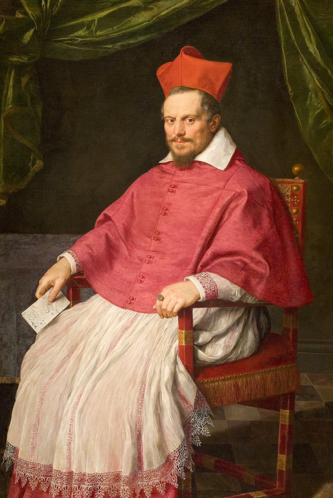 L'image représente un homme en position assise, vêtu d'une tenue ecclésiastique richement ornée. Il porte une robe rouge avec des détails en blanc, typique des cardinaux, ainsi qu'un chapeau rouge distinctif. Ses cheveux et sa barbe sont soigneusement coiffés. L'arrière-plan est composé de draperies vertes, créant un contraste avec sa tenue, tandis que le sol est orné d'un motif en damier. L'expression de l'homme est sérieuse et contemplative.