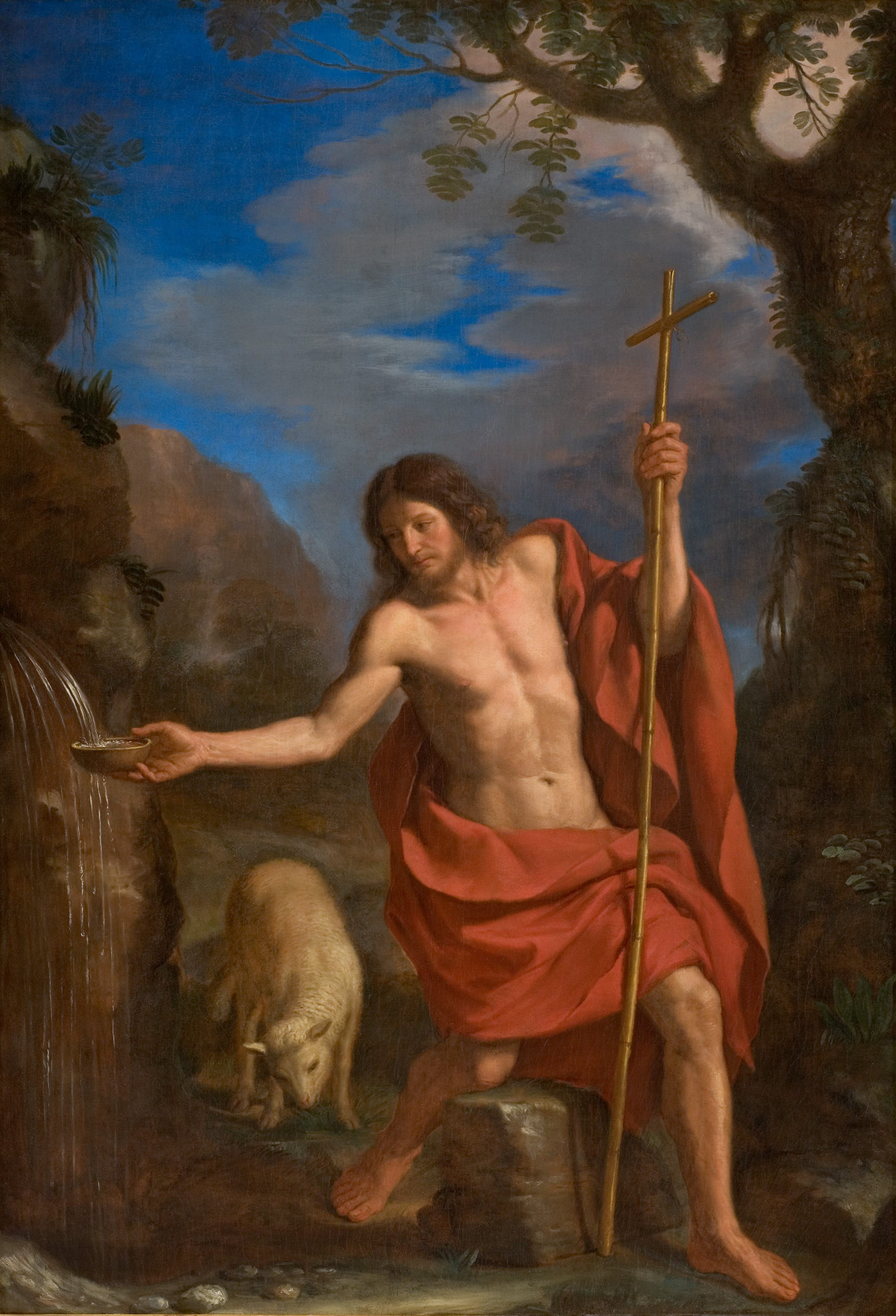 L'image représente une scène religieuse avec un homme, souvent identifié comme une figure chrétienne, agenouillé près d'un cours d'eau. Il est vêtu d'un drap rouge, mettant en valeur sa silhouette. Dans une main, il tient une croix, tandis que l'autre semble se pencher vers l'eau, suggérant une action de bénédiction ou d'offrande. À proximité, un mouton se trouve, symbolisant souvent le peuple ou les fidèles dans un contexte spirituel. L'arrière-plan présente des montagnes et des arbres sous un ciel bleu, créant une atmosphère paisible et naturelle.