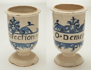 L'image montre un récipient en céramique, probablement un vase ou une coupe. Il a une base élargie et est décoré de motifs peints en bleu sur un fond clair. Sur le récipient, on peut lire deux inscriptions : "Infection" sur un côté et "Dementia" de l'autre, toutes deux entourées de décorations florales et de visages stylisés. Ce type de pièce pourrait avoir un usage historique ou médical.