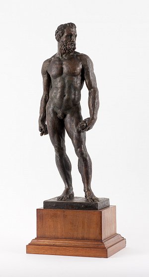 L'image représente une sculpture en bronze d'une figure masculine nue, debout sur un socle en bois. La sculpture montre un homme musclé avec une barbe, présentant des détails réalistes dans sa posture et ses proportions. Le modèle est tourné légèrement sur le côté, ce qui donne une impression de dynamisme et de mouvement. La finition en bronze lui confère une texture riche et un aspect lumineux.